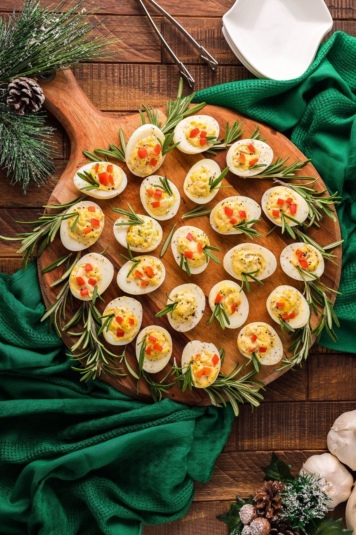 Christmas Deviled Eggs garnished with herbs and diced vegetables are served on a round wooden board, making a festive holiday appetizer perfect for your Christmas party.