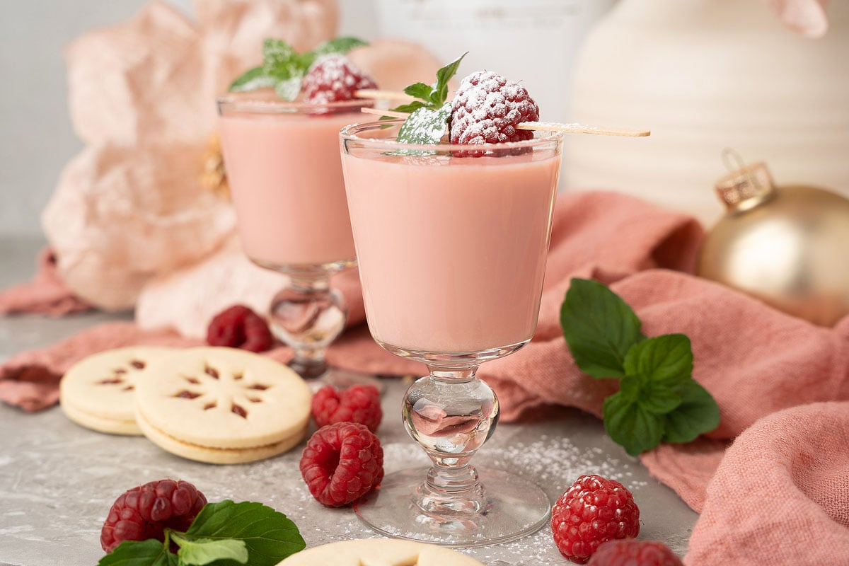 Two glasses of milk with raspberries and cookies, perfect for a holiday cocktail or Christmas shots recipe.