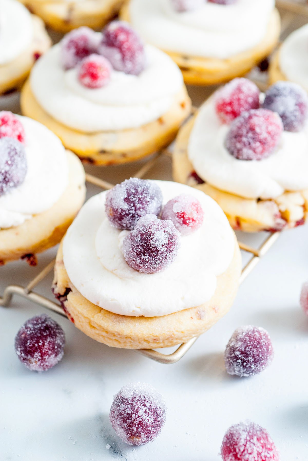 Sparkling Frosted Cranberry Cookies topped with white frosting and sugared cranberries cool on a rack, with sparkling cranberries scattered nearby.