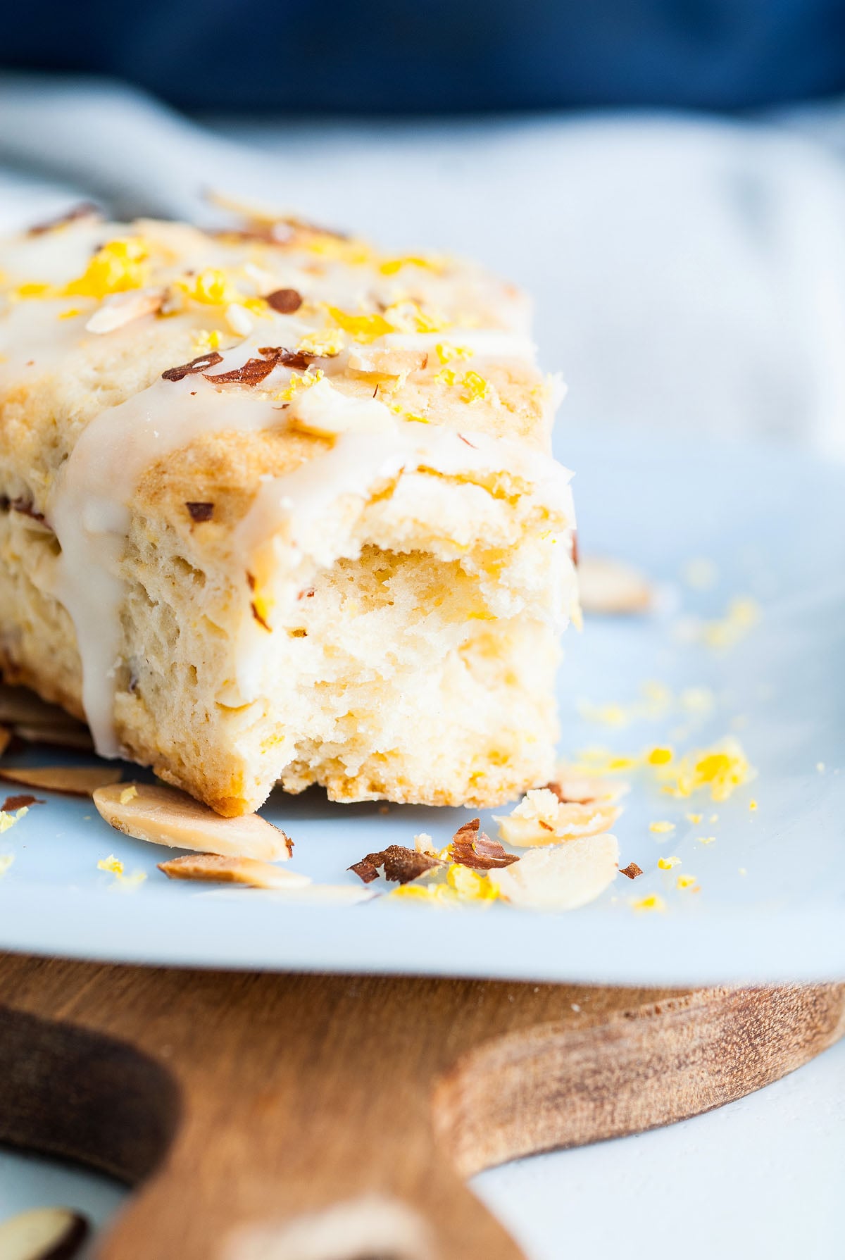 A glazed Lemon Almond Scone topped with sliced almonds and lemon zest sits on a light blue plate—a delightful treat for anyone seeking an easy scone recipe.