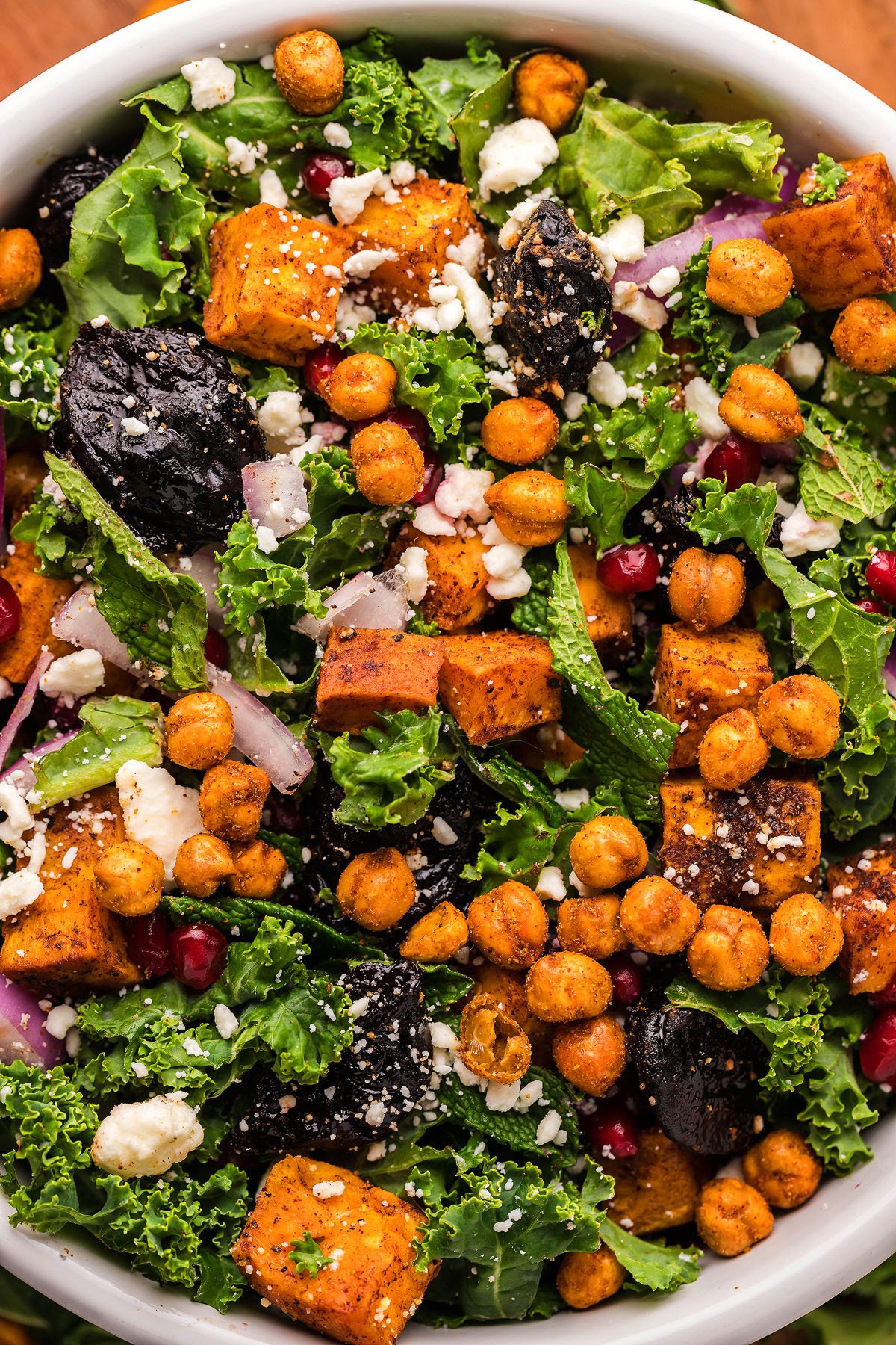 A vibrant sweet potato kale salad featuring roasted chickpeas, dried plums, feta cheese, and pomegranate seeds.