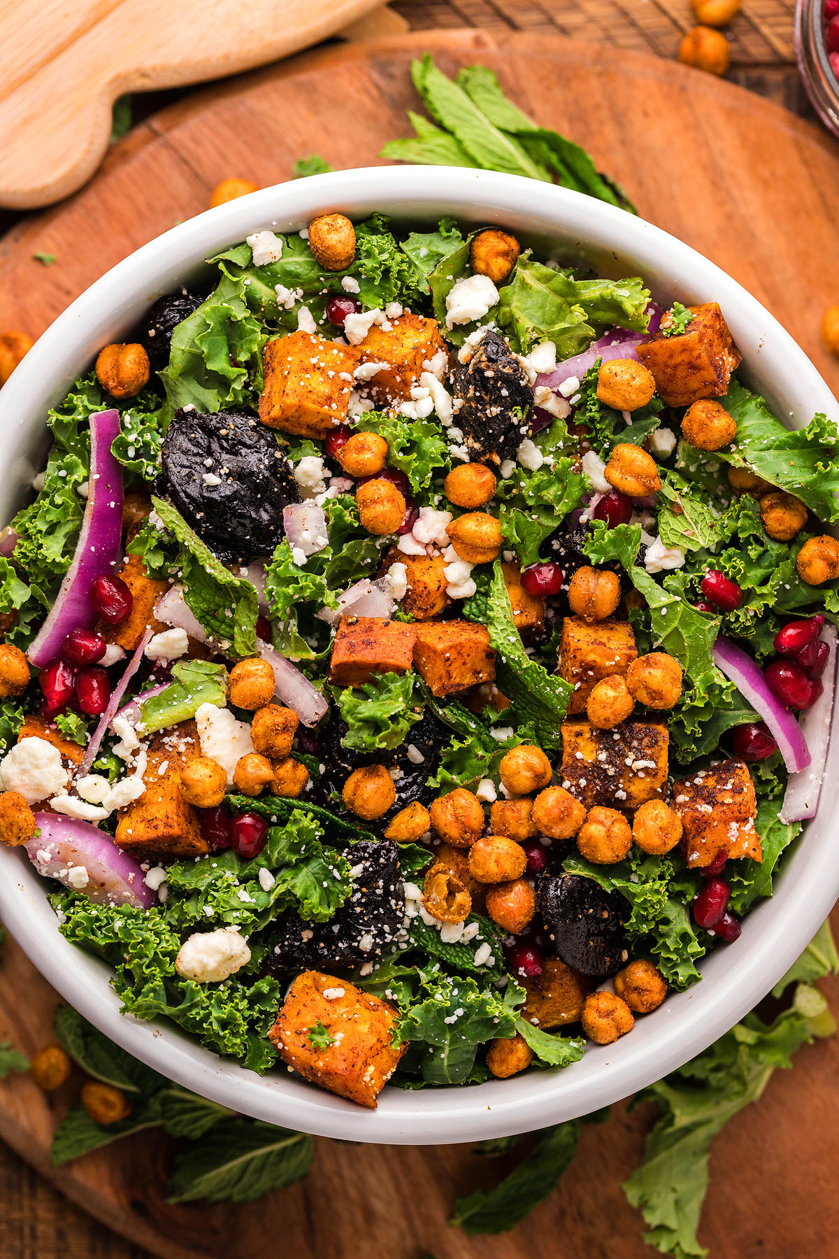 A vibrant sweet potato kale salad featuring roasted chickpeas, red onion, feta cheese, and pomegranate seeds creates a fresh and satisfying bowl.