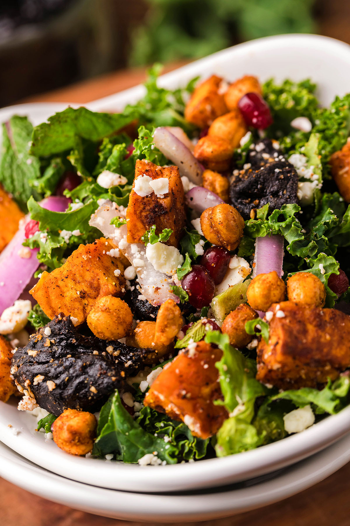 A vibrant sweet potato kale salad with roasted sweet potatoes, chickpeas, feta cheese, onions, and pomegranate seeds for a delicious twist on classic kale salad.