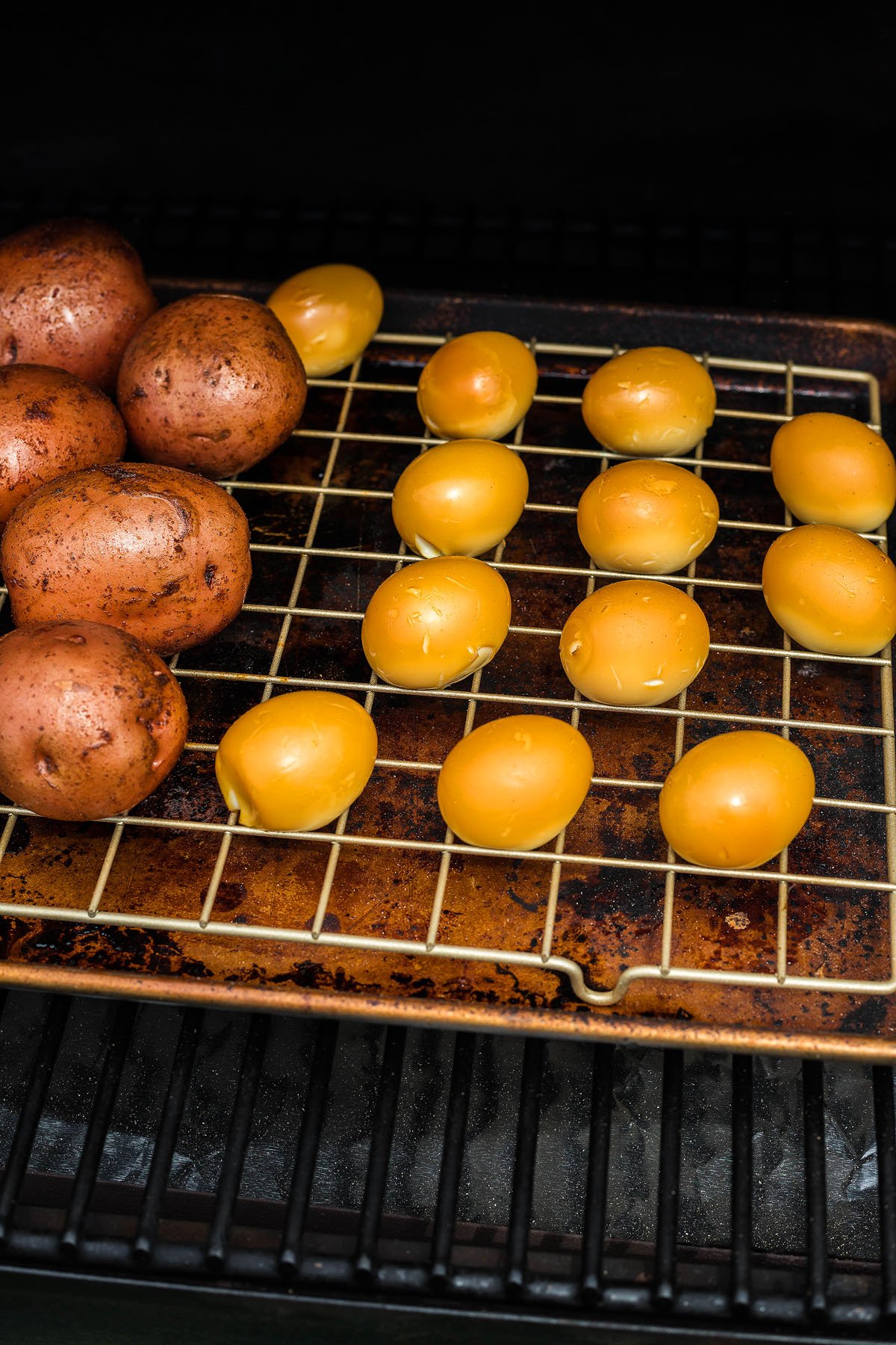 Potatoes and yellow cherry tomatoes on a grill rack, ready to be cooked for a flavorful Smoked Potato Salad on your Traeger grill.