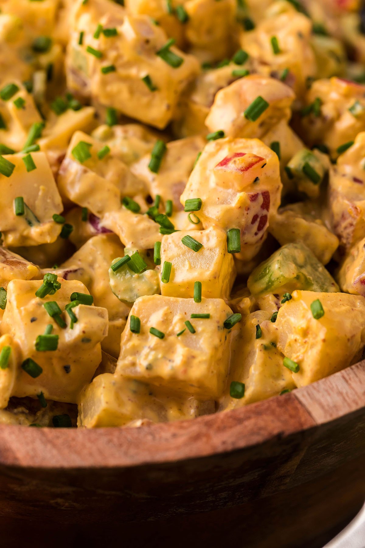 Close-up of creamy Smoked Potato Salad with chopped chives, red onion, celery, smoked potatoes and smoked hard boiled eggs in a wooden bowl.