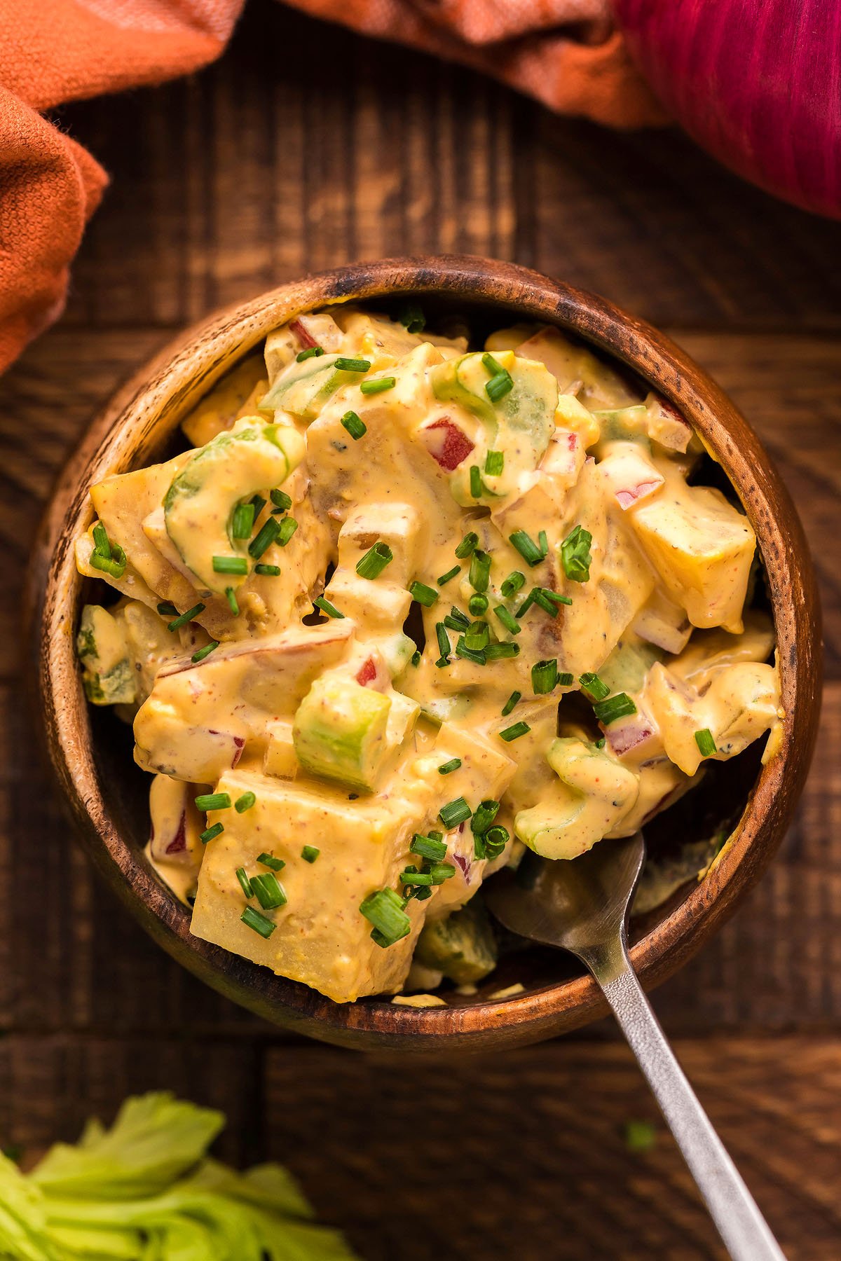 A bowl of creamy smoked potato salad with chives on top, served with a spoon on a wooden table, brings savory flavor from the pellet smoker.