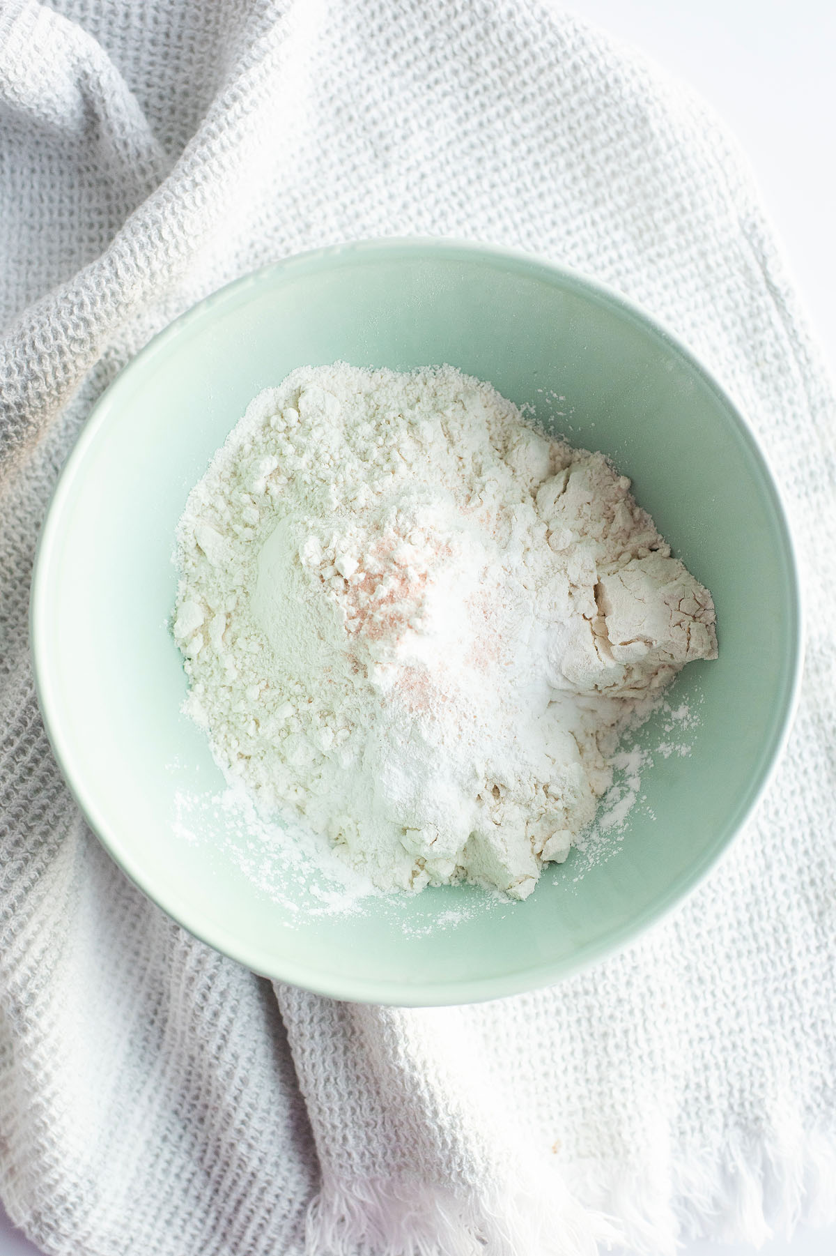 A green bowl with flour and baking powder on a white textured cloth, ready for making delicious caramel stuffed chocolate cookies.