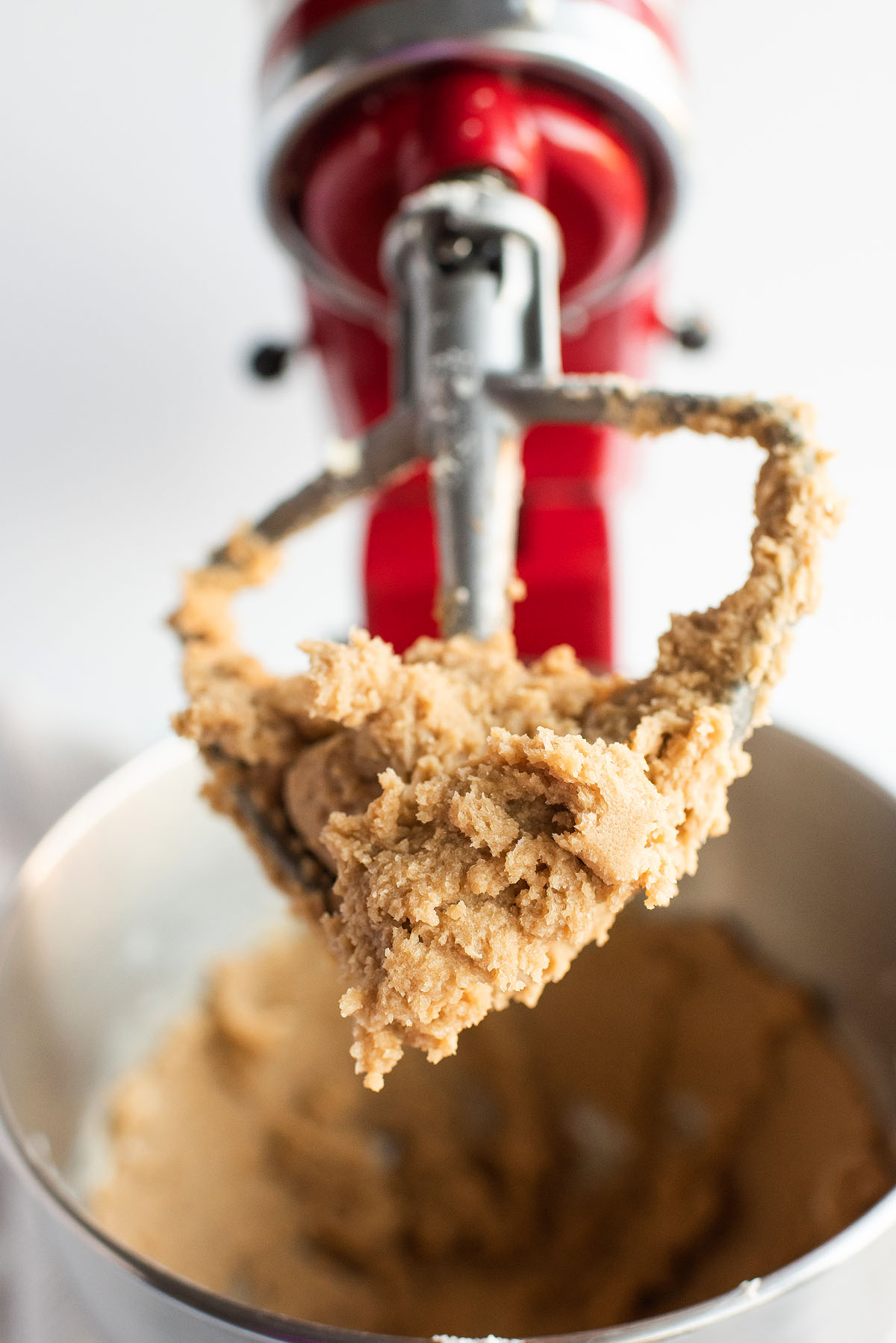 Close-up of caramel stuffed chocolate cookie dough on a mixer paddle, ready to become irresistible caramel filled cookies in a red stand mixer with a metal bowl.