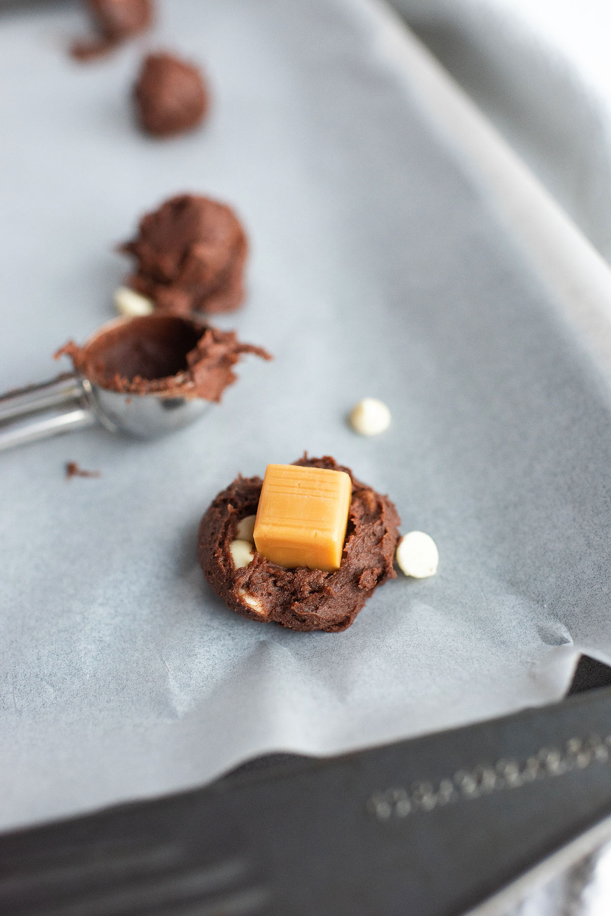 A scoop of chocolate cookie dough with a caramel square on top, sitting on parchment paper—perfect for baking delicious Caramel Stuffed Chocolate Cookies.