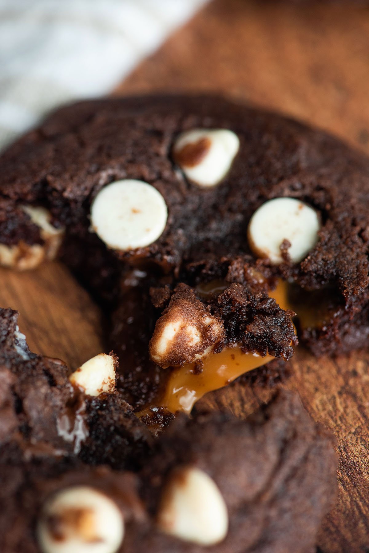 A close-up of Caramel Stuffed Chocolate Cookies with white chocolate chips and gooey caramel filling on a wooden surface.