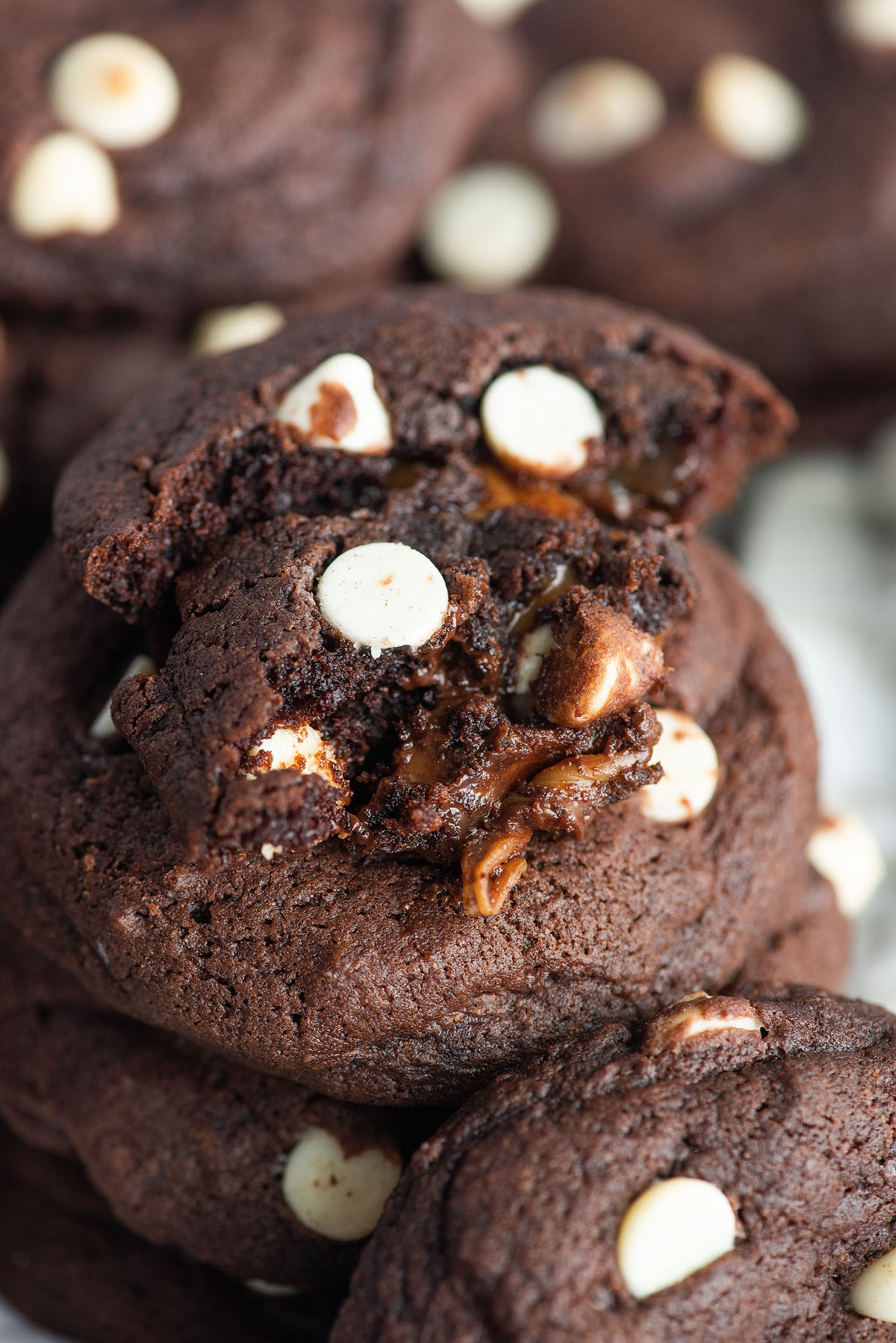 Close-up of Caramel Stuffed Chocolate Cookies with white chocolate chips, one broken to reveal a gooey, melty caramel center.