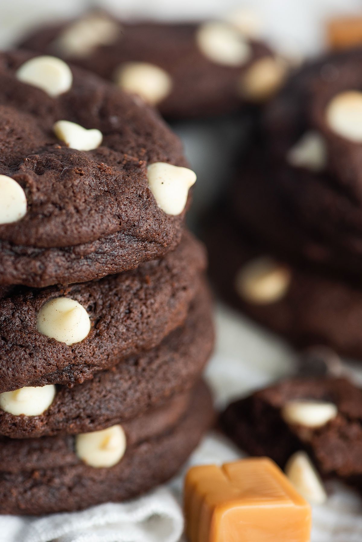 Close-up of Caramel Stuffed Chocolate Cookies with white chocolate chips, stacked beside rich caramel squares.