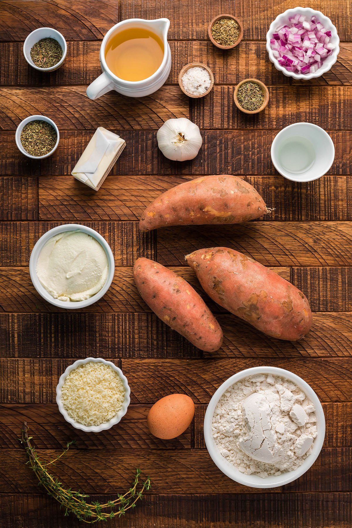 Ingredients for cooking—sweet potatoes, egg, flour, butter, spices, broth, garlic, onions, ricotta, and cheese on wood—perfect for crafting a homemade potato gnocchi recipe or delicious Sweet Potato Gnocchi with roasted garlic sauce.