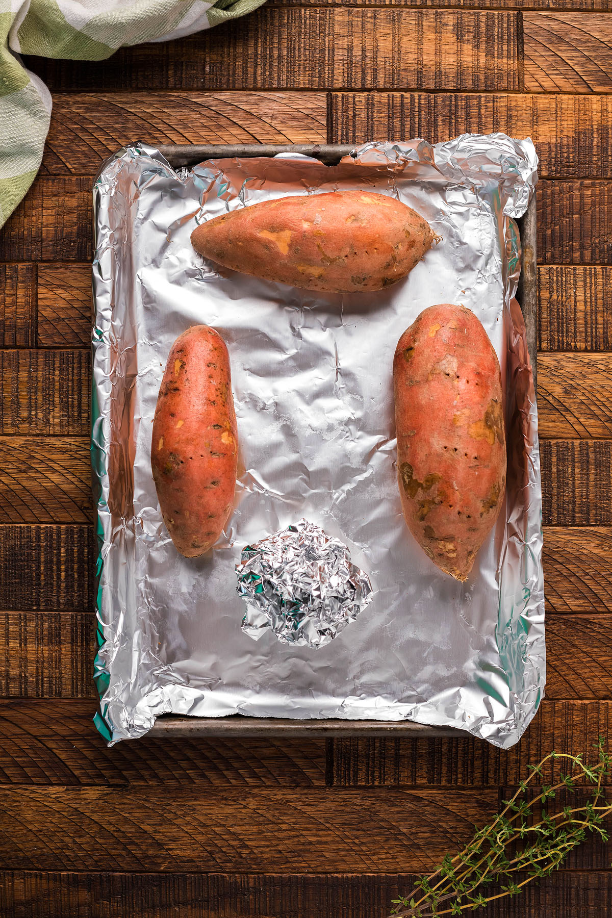 Three sweet potatoes and a ball of foil on a foil-lined baking tray, ready to be baked as the first step in a delicious homemade potato gnocchi recipe.
