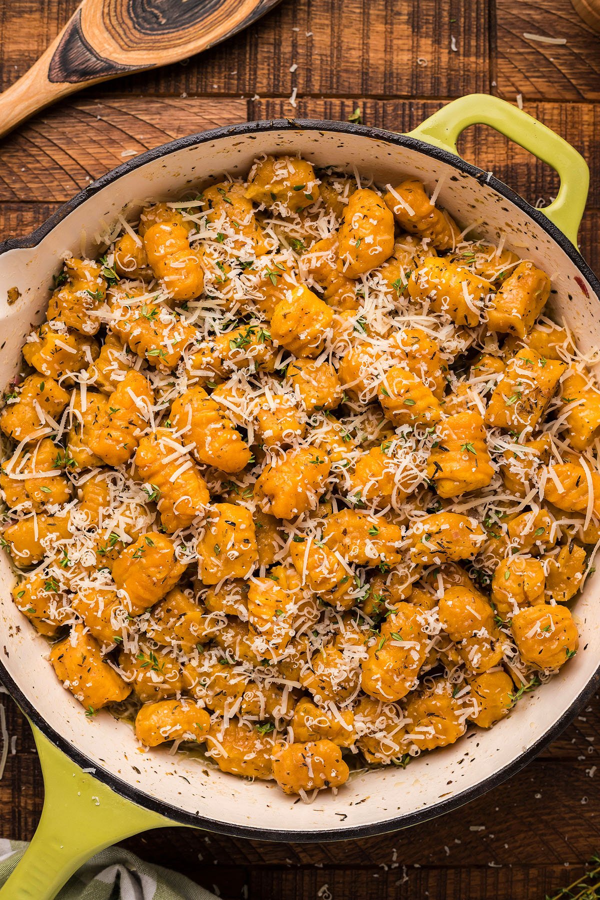 A pan of homemade potato gnocchi topped with grated cheese and herbs sits on a rustic wooden table, ready to be enjoyed with a rich roasted garlic sauce.