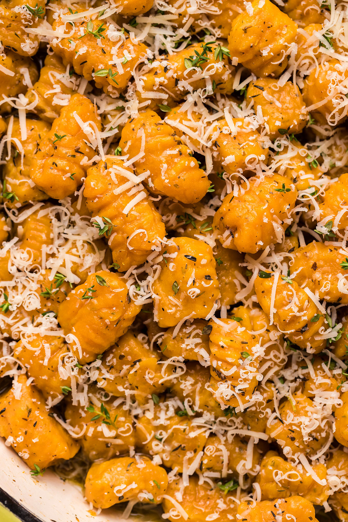 Close-up of sweet potato gnocchi topped with shredded cheese, fresh herbs, and finished with a rich roasted garlic sauce.