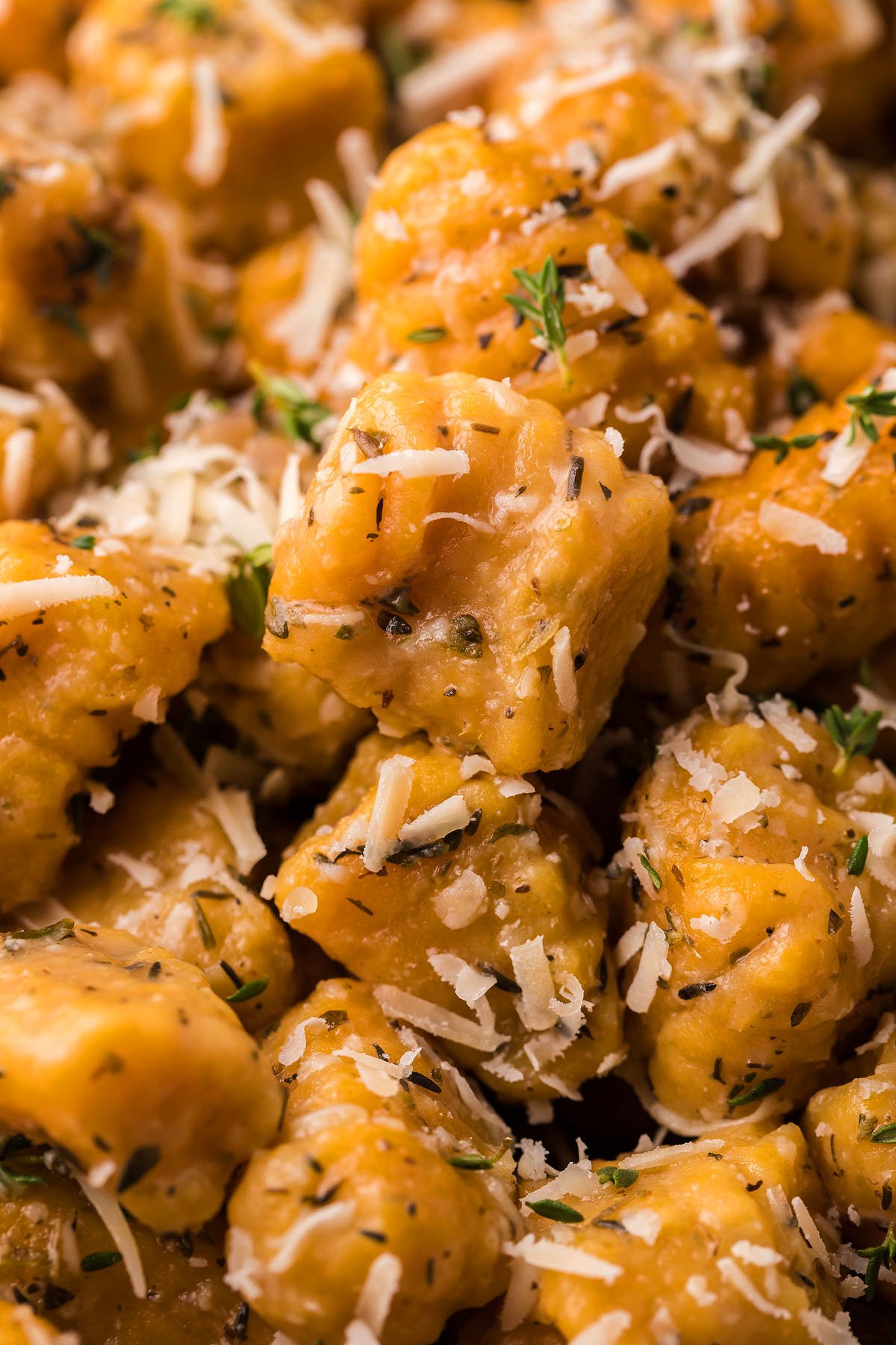 Close-up of golden sweet potato gnocchi topped with grated cheese, herbs, and seasoning, finished with a drizzle of roasted garlic sauce.