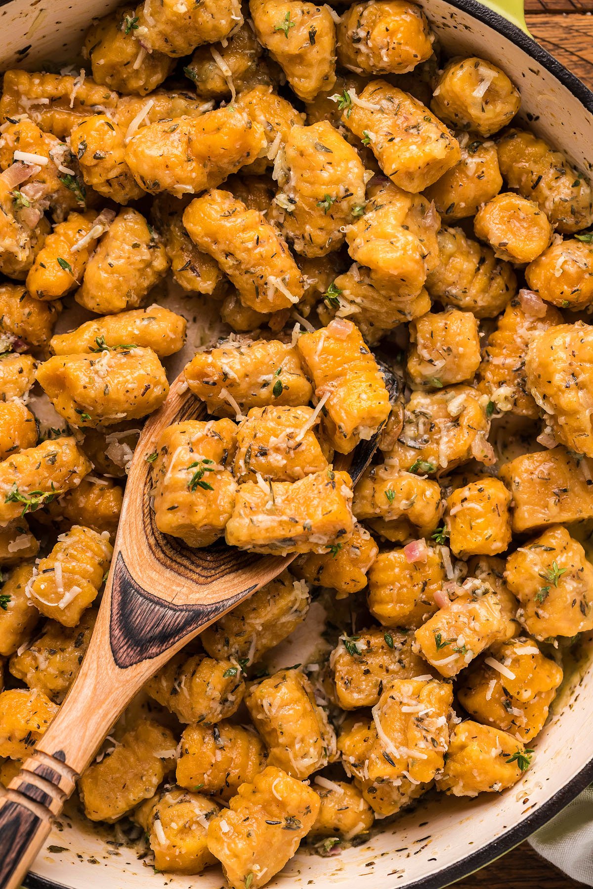 Close-up of homemade potato gnocchi recipe with herbs and grated cheese, stirred with a wooden spoon in a pan.