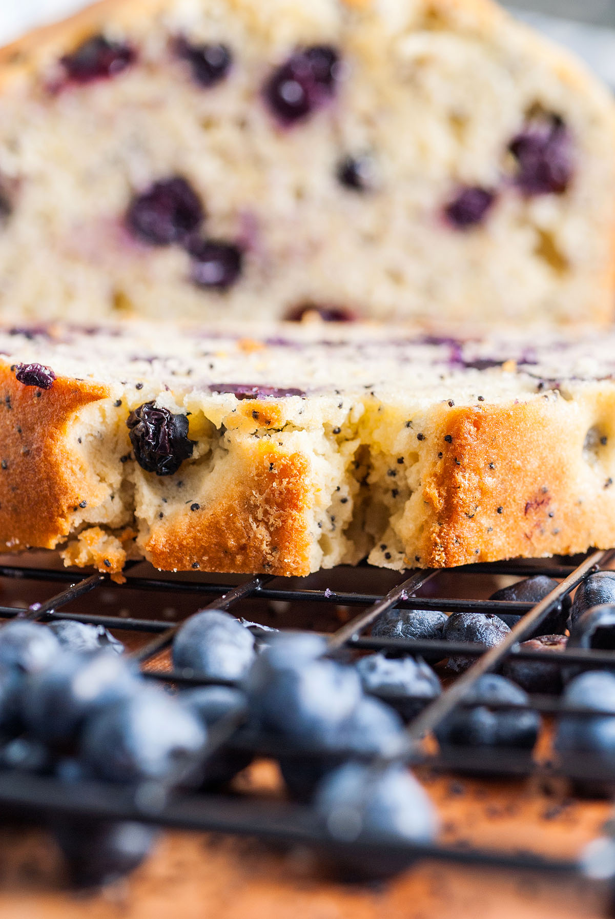 Close-up of Lemon Blueberry Poppy Seed Loaf with fresh blueberries on a cooling rack.