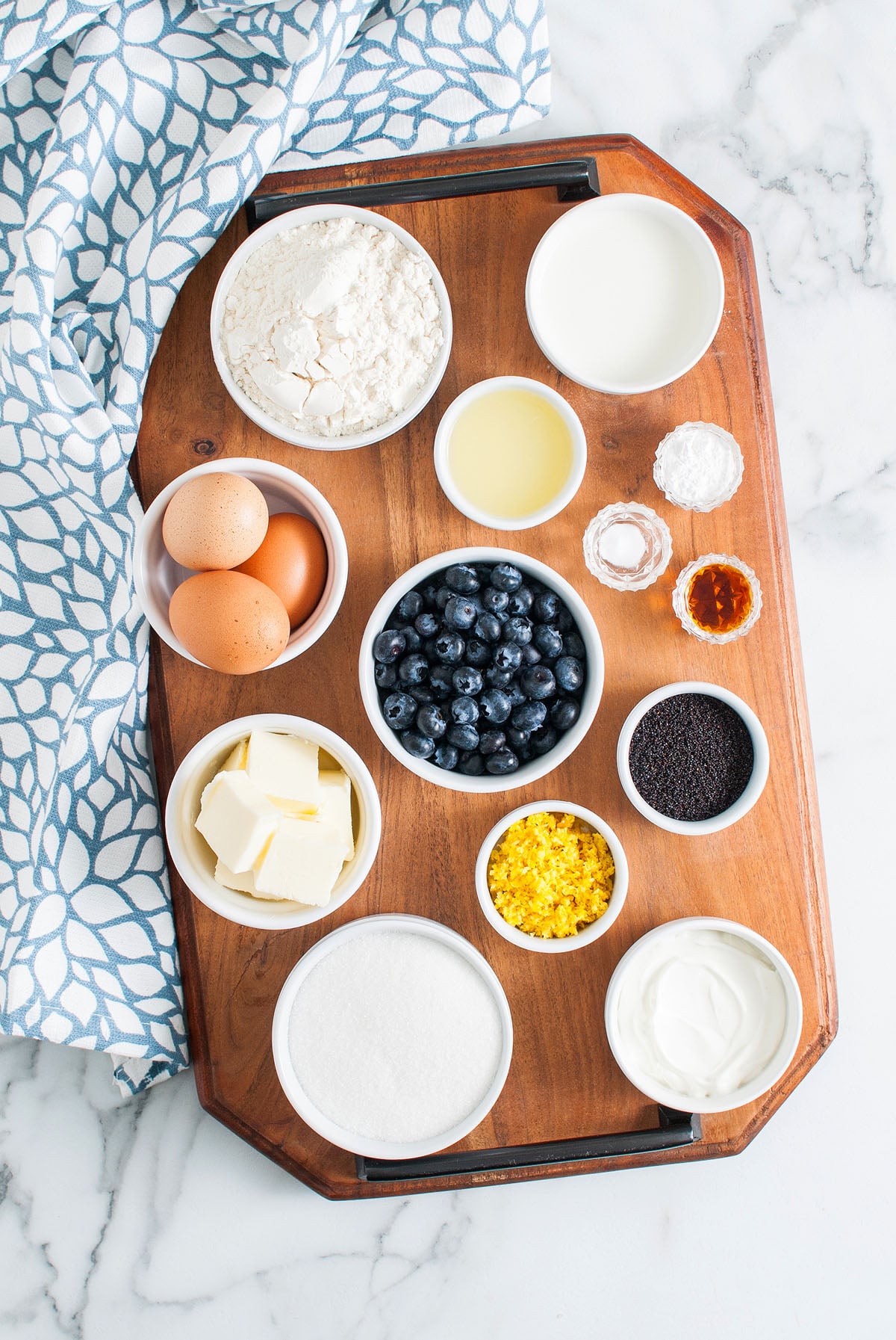A wooden tray with bowls of flour, blueberries, eggs, butter, sugar, milk, and other baking ingredients&mdash;perfect for making a delicious Lemon Blueberry Poppy Seed Loaf.
