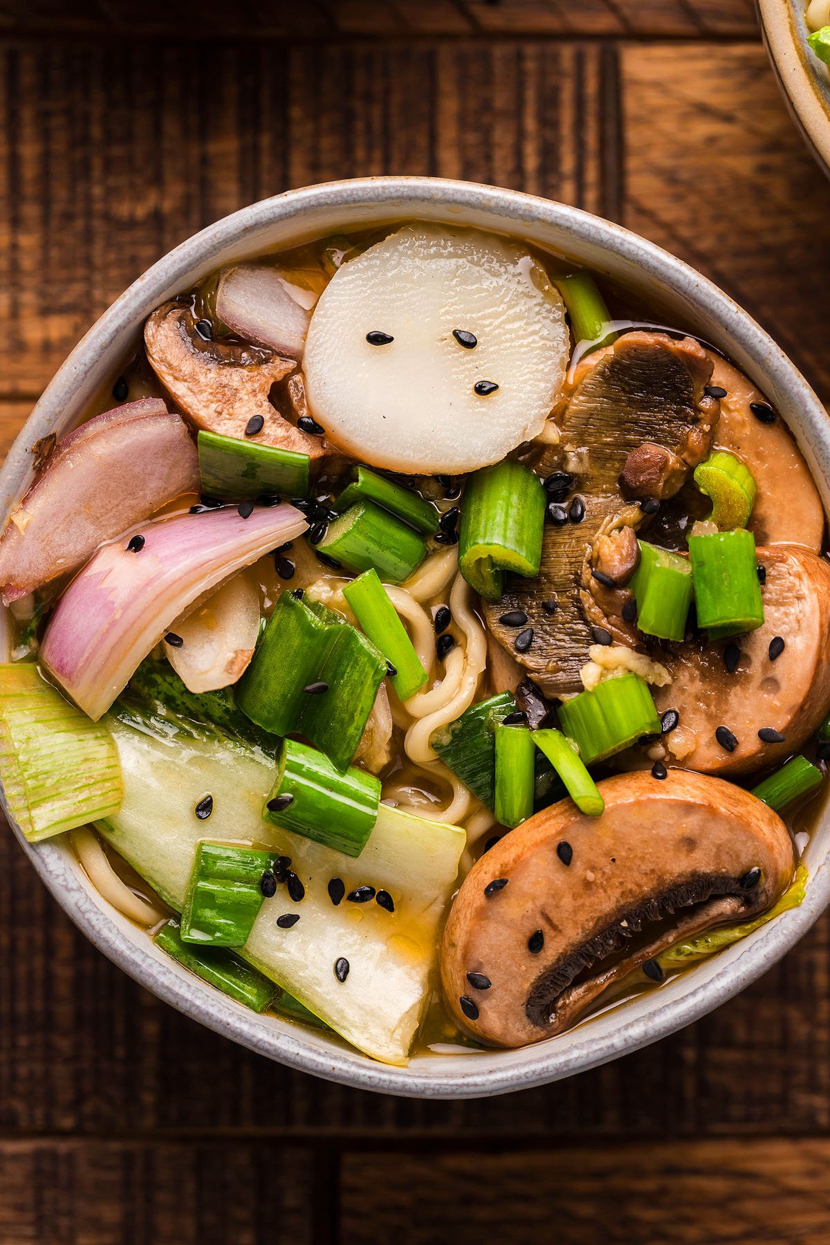 Bowl of Miso Mushroom Ramen Soup with mushrooms, green onions, bok choy, and black sesame seeds on a wooden table—a cozy gluten free vegan ramen perfect for any night.