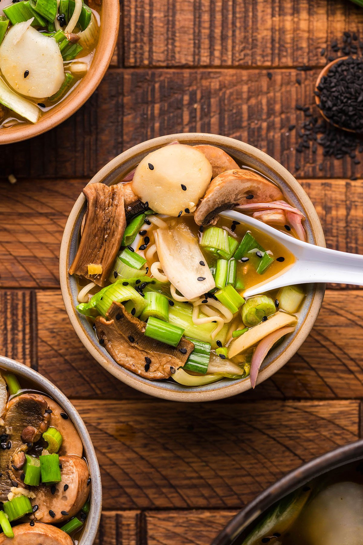 A bowl of Miso Mushroom Ramen Soup with mushrooms, green onions, and black sesame seeds on a wooden table—an inviting gluten free vegan ramen for any miso ramen recipe lover.