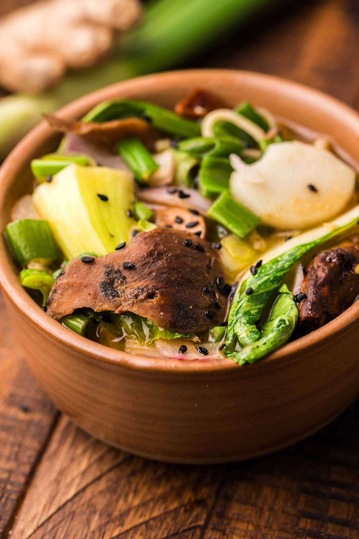 A bowl of Miso Mushroom Ramen Soup with bok choy, scallions, and sesame seeds sits on a wooden table—a comforting gluten free vegan ramen perfect for any day.