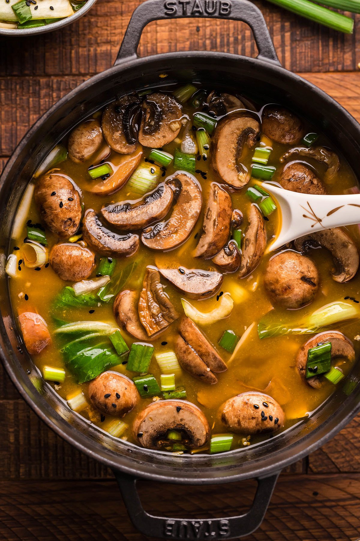 A pot of Miso Mushroom Ramen Soup with chopped green onions and a ladle sits on a wooden table, perfect for those seeking a cozy, gluten free vegan ramen experience.