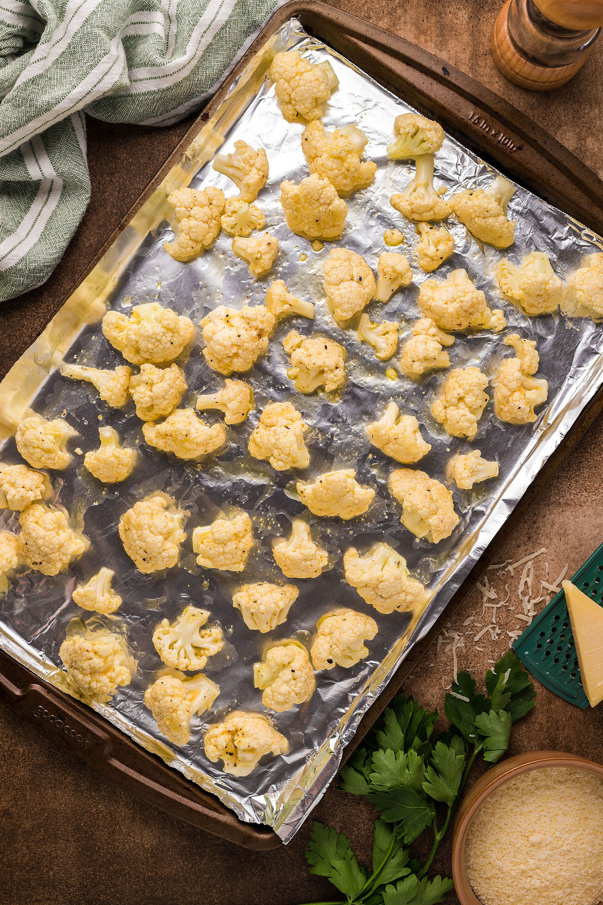 Cauliflower florets on a foil-lined baking sheet, ready for roasting for an easy weeknight dinner like Roasted Cauliflower Carbonara, with cheese and herbs nearby to create a delicious cauliflower sauce.