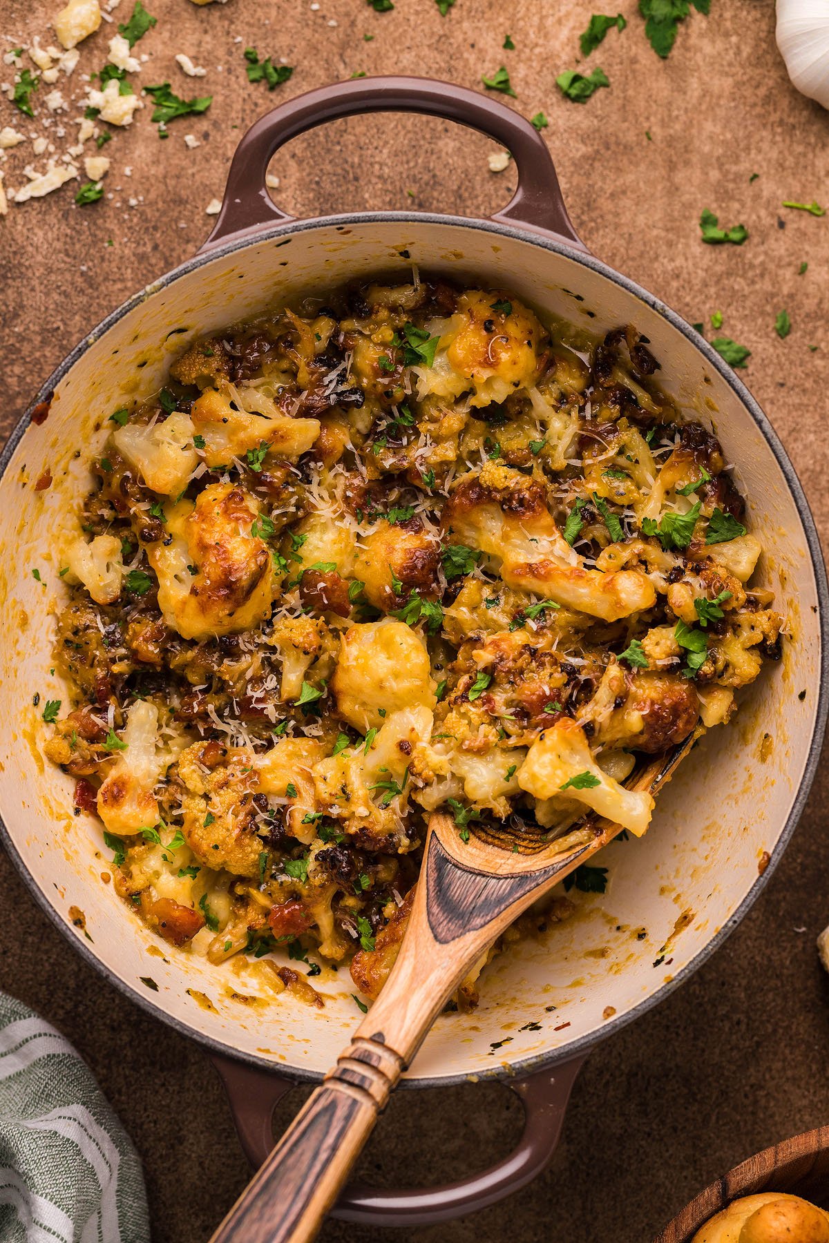 Baked cauliflower with crispy, golden edges and herbs in a round casserole dish, perfect as an easy weeknight dinner or served with creamy cauliflower sauce; a wooden spoon rests beside it.