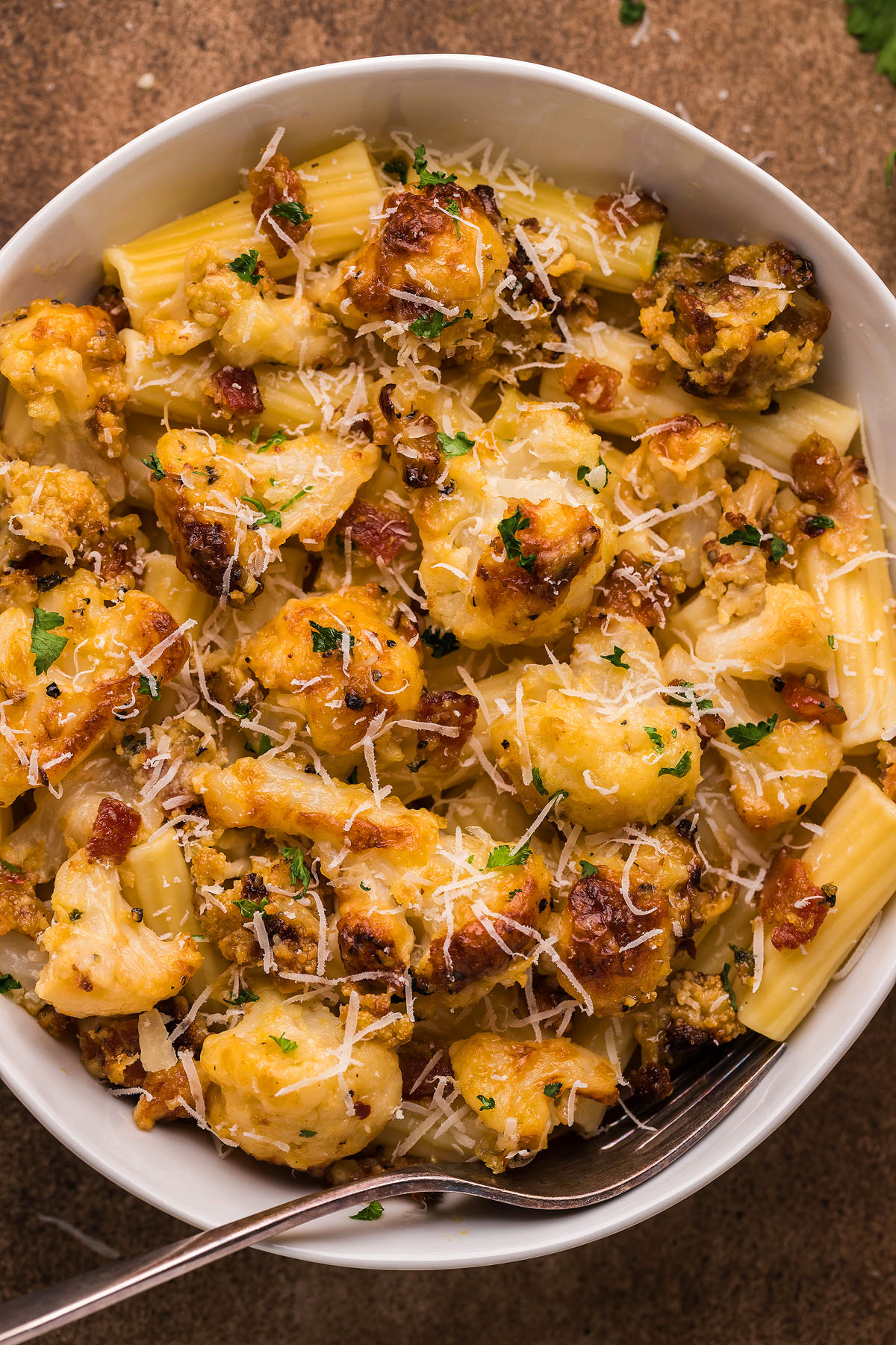 A bowl of Roasted Cauliflower Carbonara rigatoni with grated cheese and herbs, featuring a creamy cauliflower sauce—an easy weeknight dinner with a fork inside.