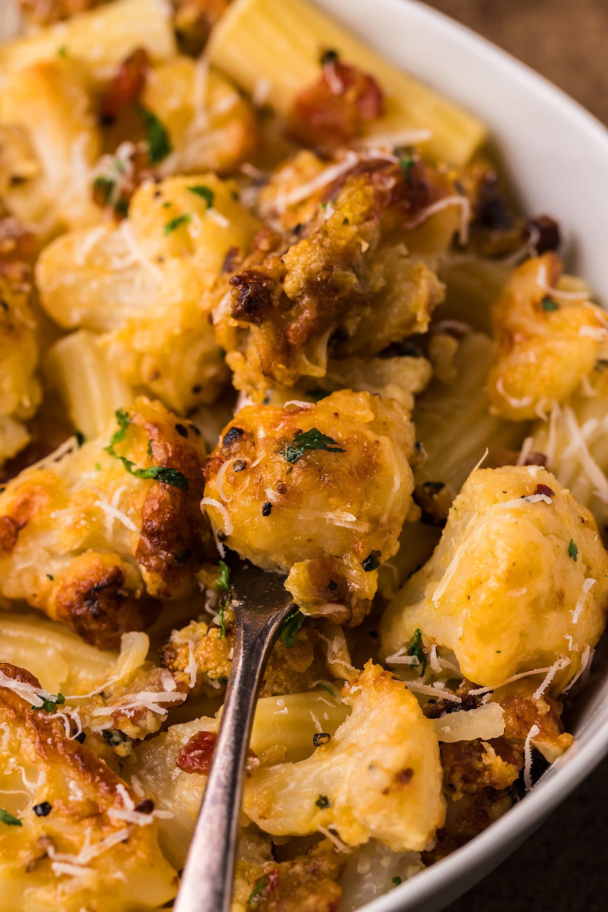 A close-up of baked rigatoni pasta with golden roasted cauliflower carbonara, fresh herbs, and grated cheese in a white bowl—an easy weeknight dinner bursting with flavor.