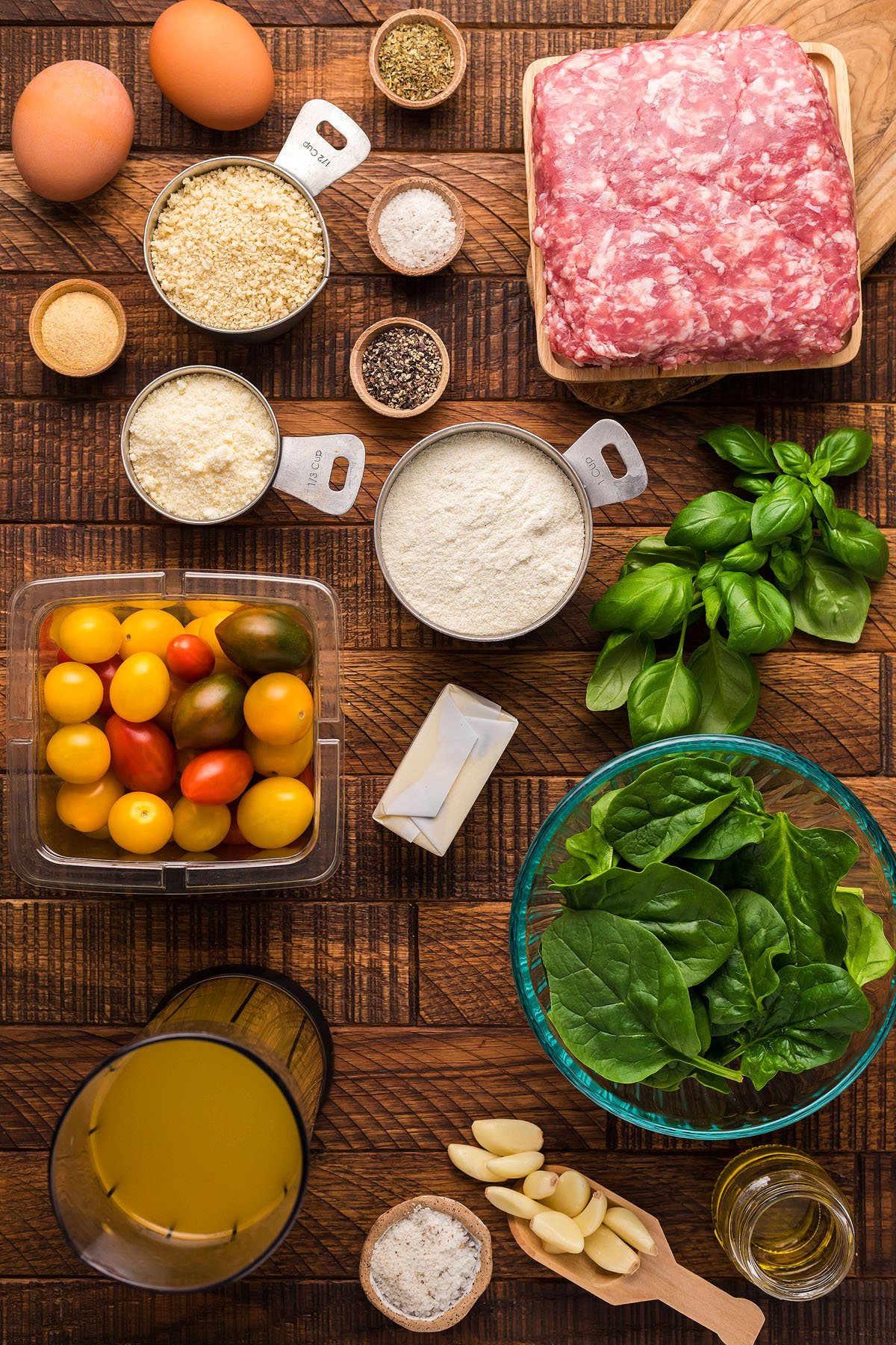 Ingredients for a gluten free meatball recipe, including ground meat, eggs, tomatoes, spinach, herbs, and seasonings on a wooden surface—perfect for exploring new Italian meatball dinner ideas.