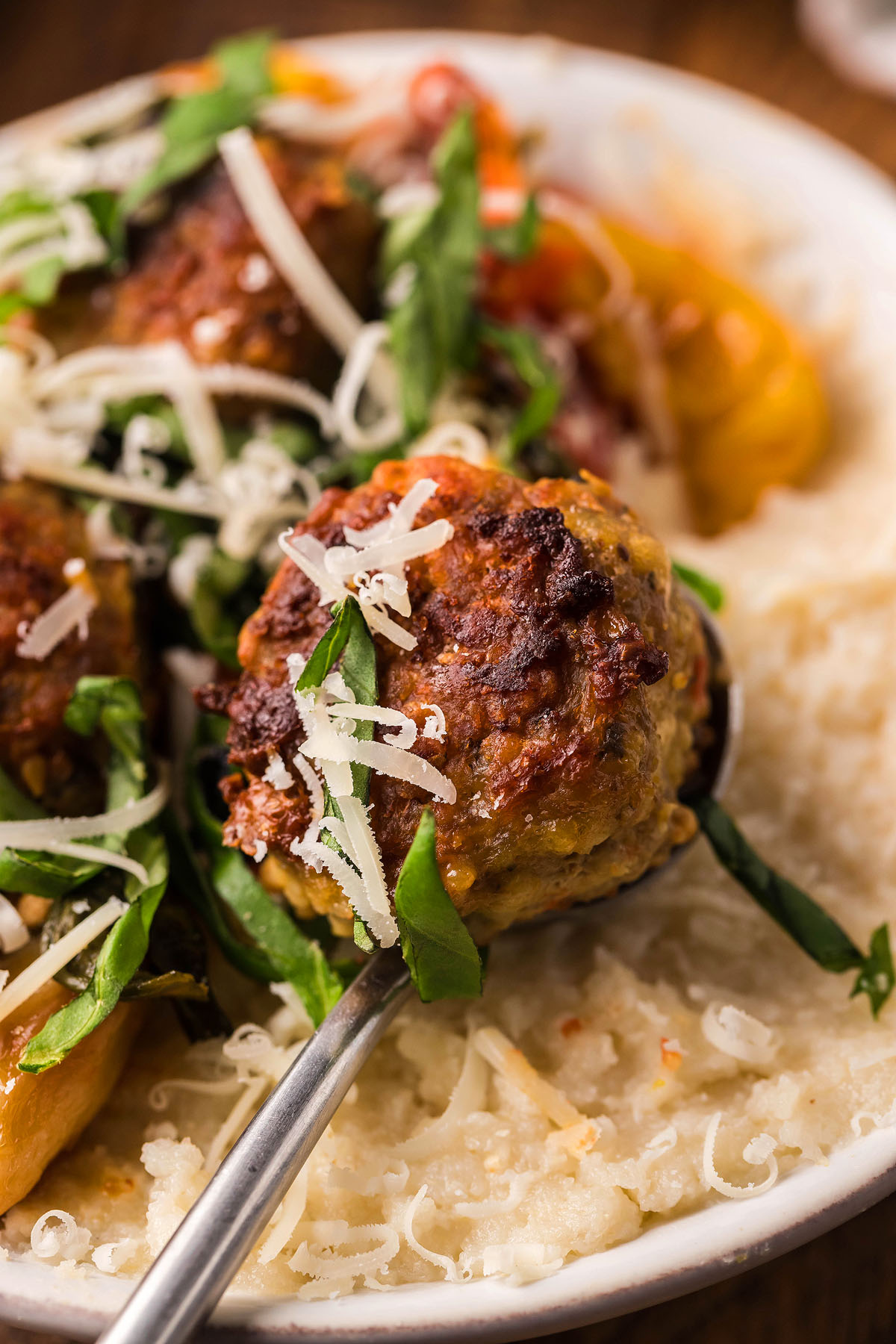 A close-up of a spoonful of meatball with grated cheese and herbs over creamy mashed potatoes, perfect for italian meatball dinner ideas or those seeking a gluten free meatball recipe.