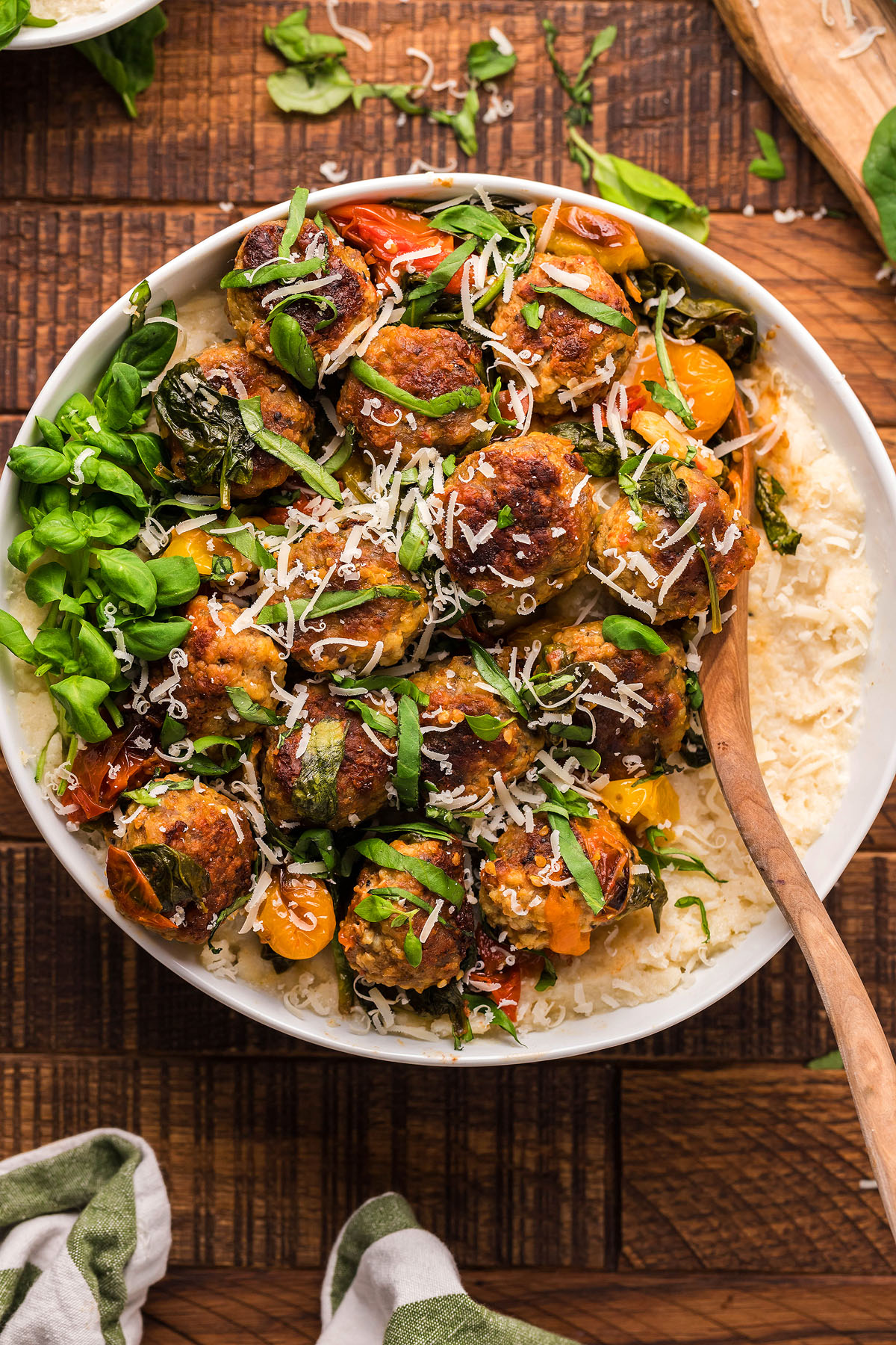 A bowl of gluten free meatball recipe with greens and tomatoes over rice, topped with shredded cheese and fresh herbs—a delicious Italian meatball dinner idea.