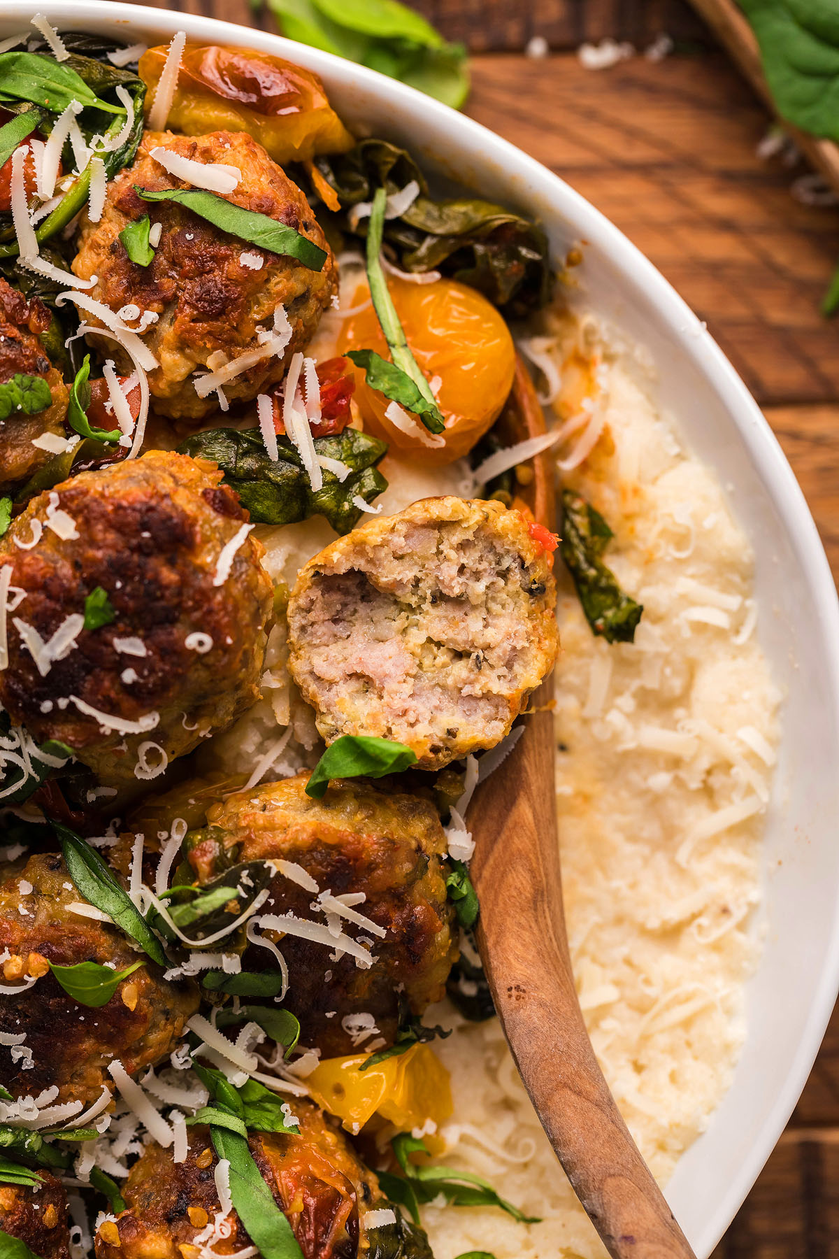 Close-up of meatballs with herbs and shredded cheese on creamy pasta, one meatball cut open on a wooden spoon—a tempting choice for italian meatball dinner ideas.