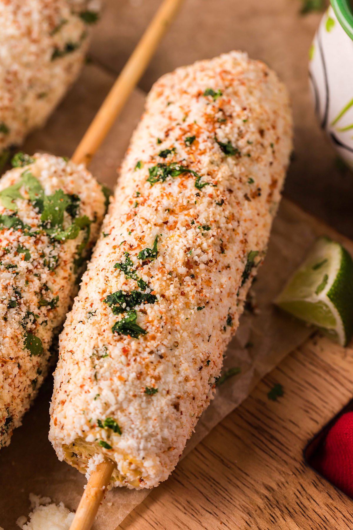 A close-up of Smoked Elote – Mexican Street Corn on a stick, coated with cheese, spices, and herbs.