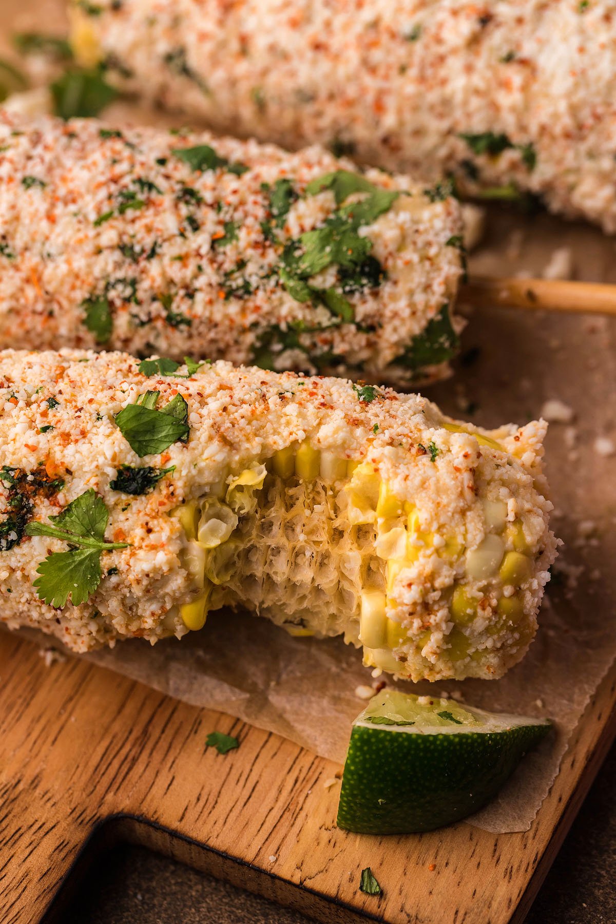 Smoked Elote – Mexican Street Corn covered in cheese and spices, with a bite taken out, and garnished with fresh cilantro.