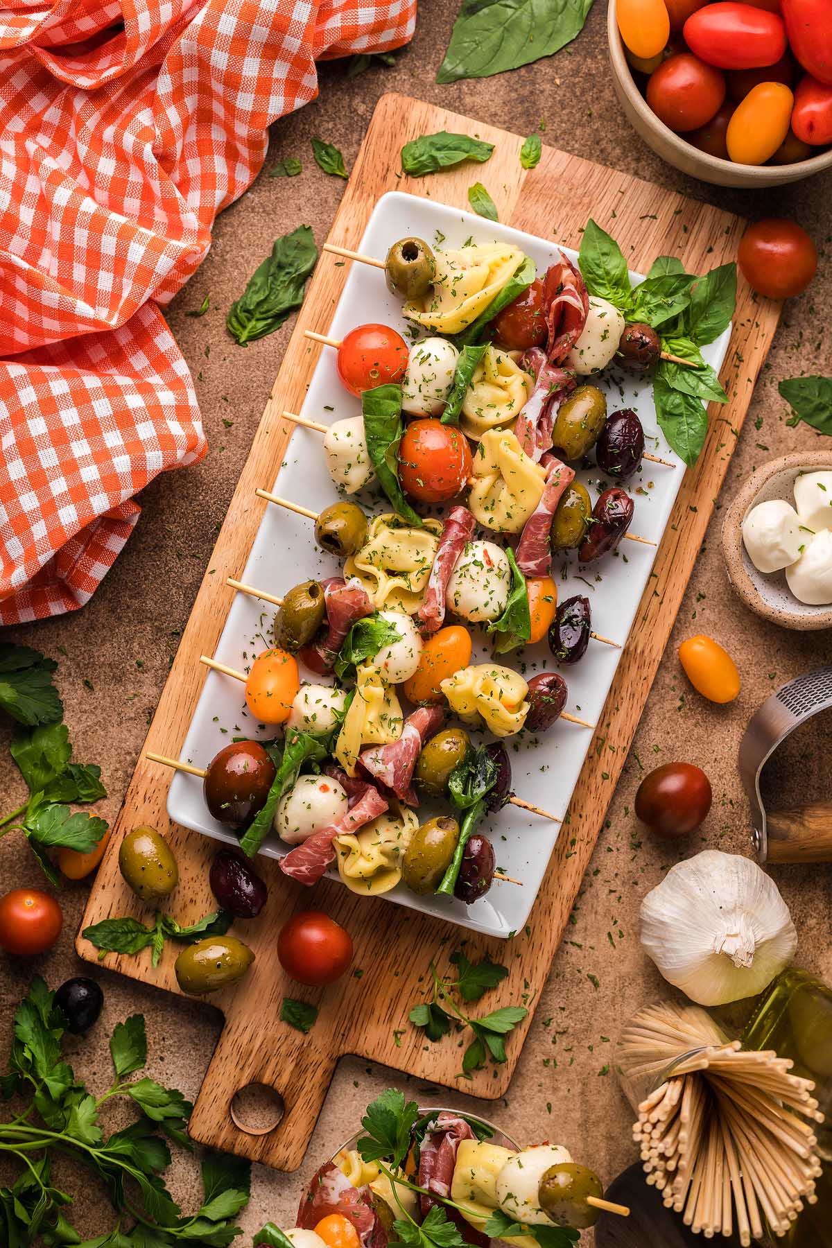 Antipasto skewers with tortellini, mozzarella, olives, tomatoes, and basil on a platter, surrounded by fresh ingredients&mdash;perfect for those looking for delicious Italian appetizer recipes.