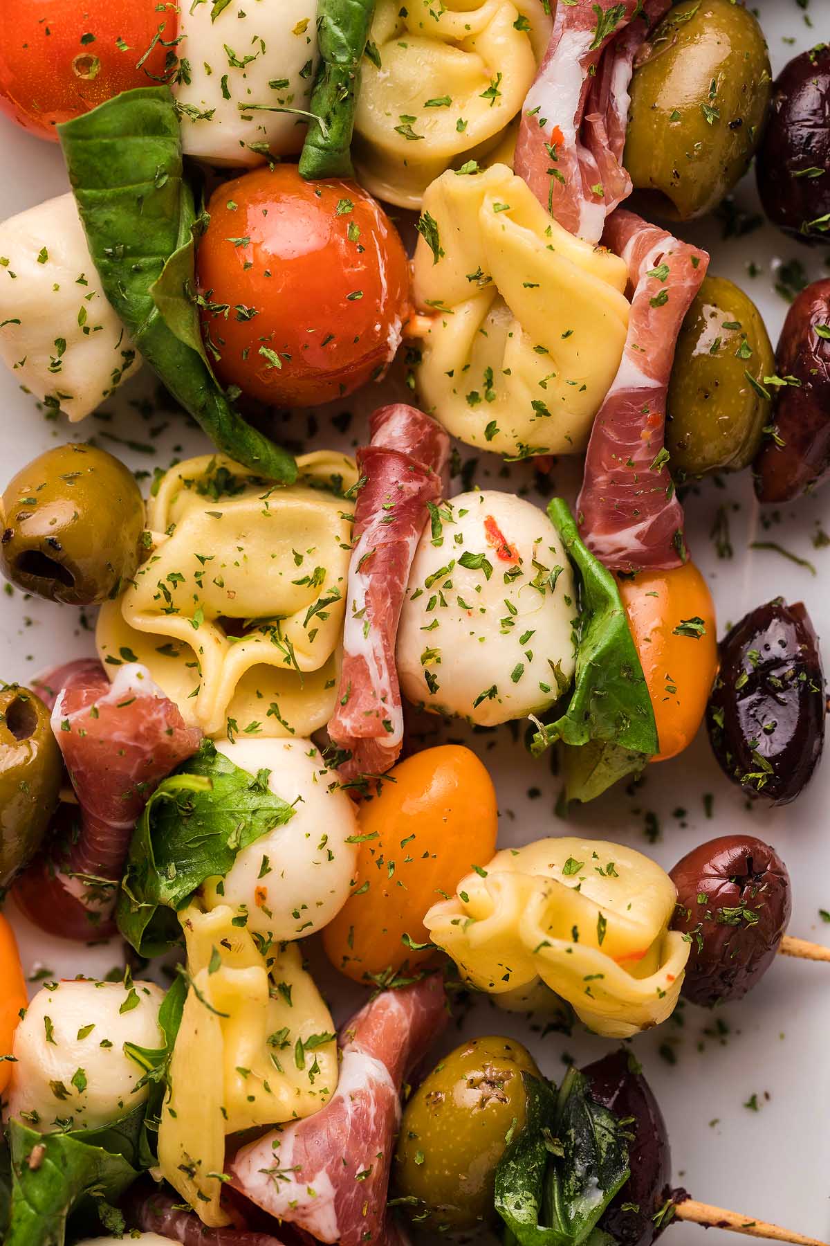Antipasto skewers with tortellini, mozzarella, tomatoes, basil, olives, and prosciutto, sprinkled with herbs&mdash;perfect for those seeking delicious Italian appetizer recipes or tasty antipasto bites.