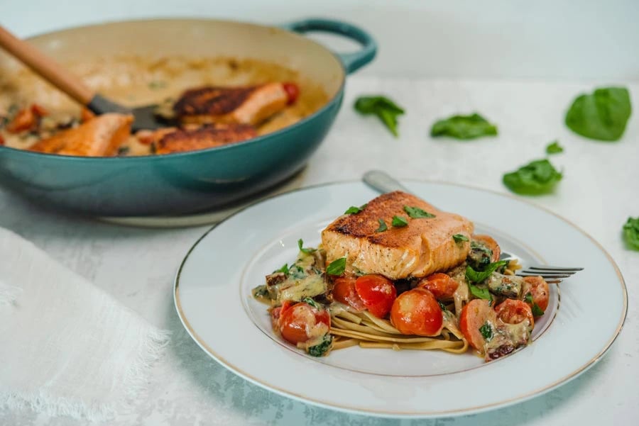 Pasta in cream sauce with tomatoes and salmon served on a plate with a fork.