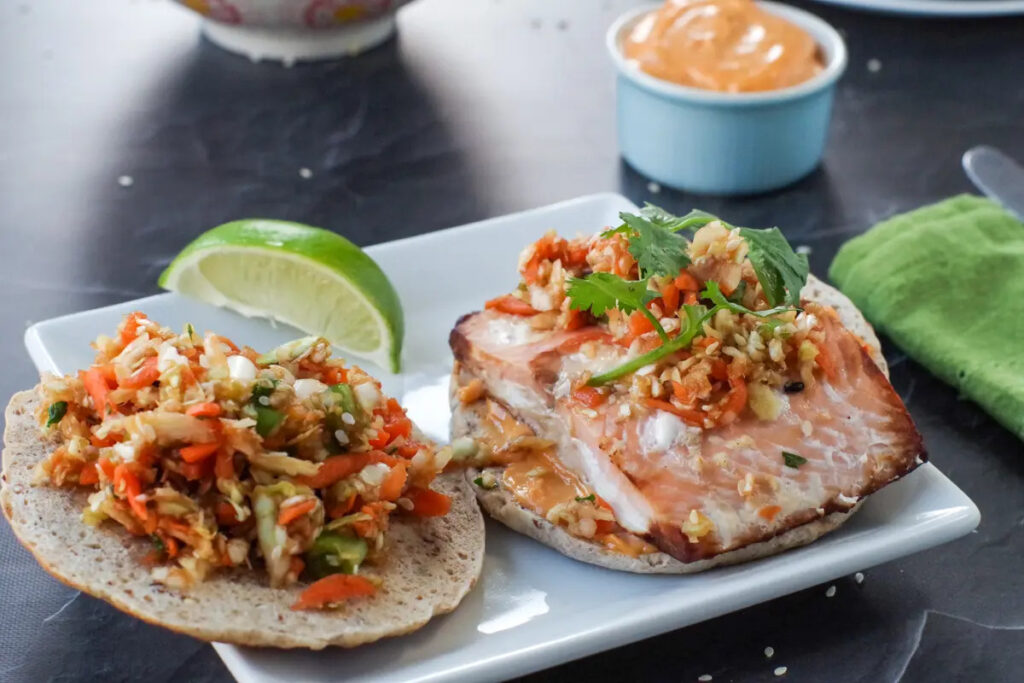 Salmon burger on a bun with coleslaw topping, served on a white plate
