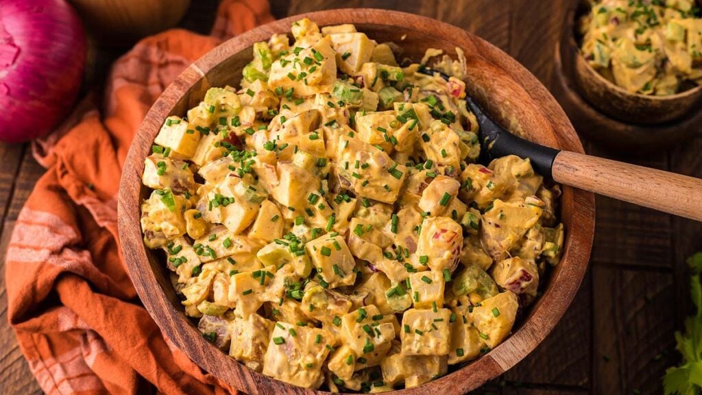 Potato salad in a wood bowl with a spoon.