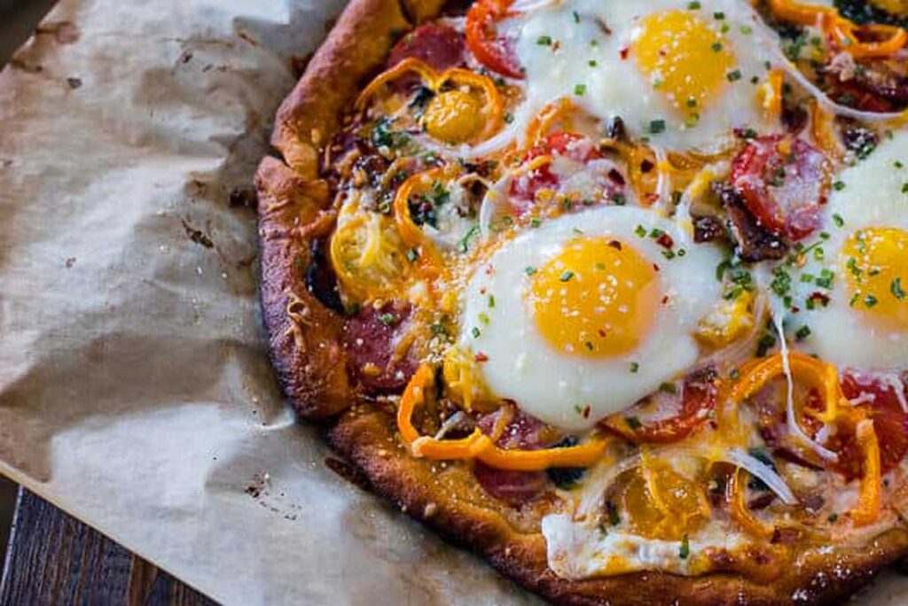Breakfast pizza with eggs on top on a white plate.