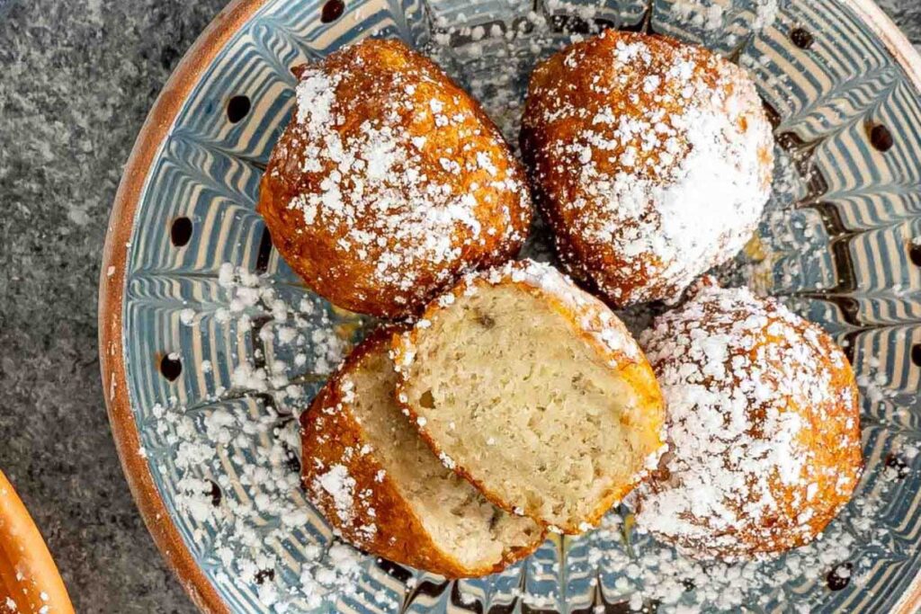 Banana apple fritters on a plate dusted with icing sugar.