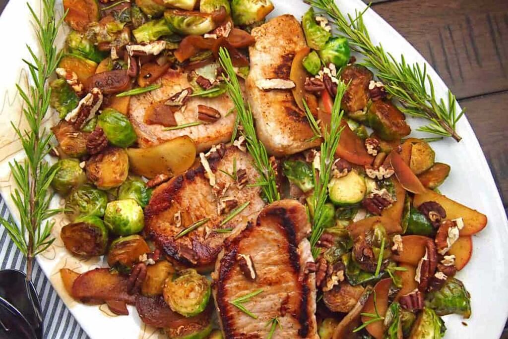 A platter of pork chops, brussels sprouts and apples