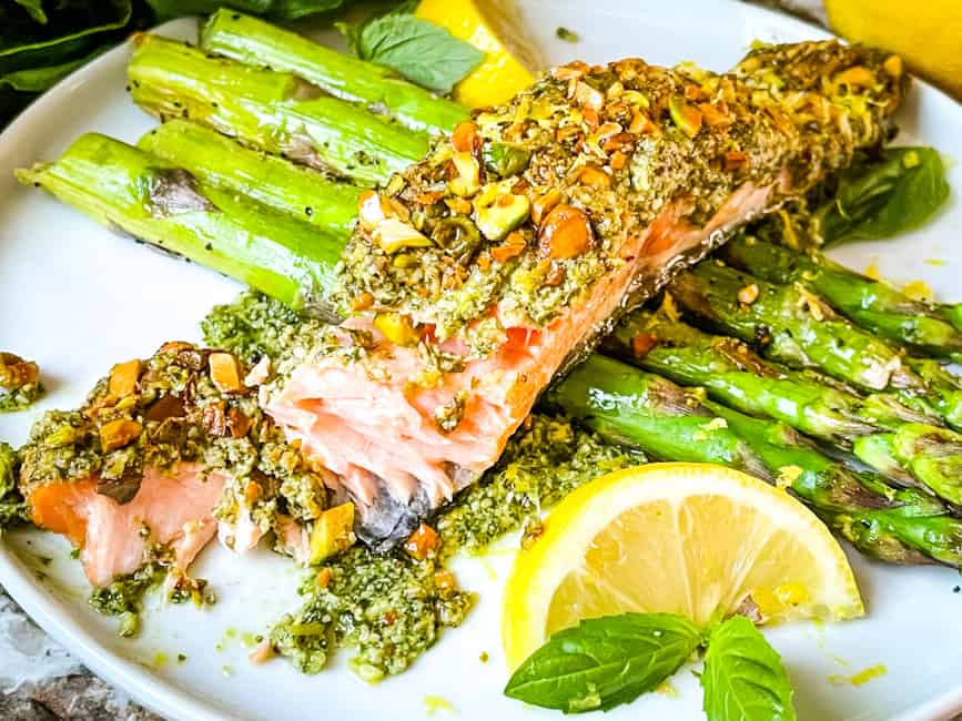 Pesto crusted salmon served over asparagus and lemons on a white plate