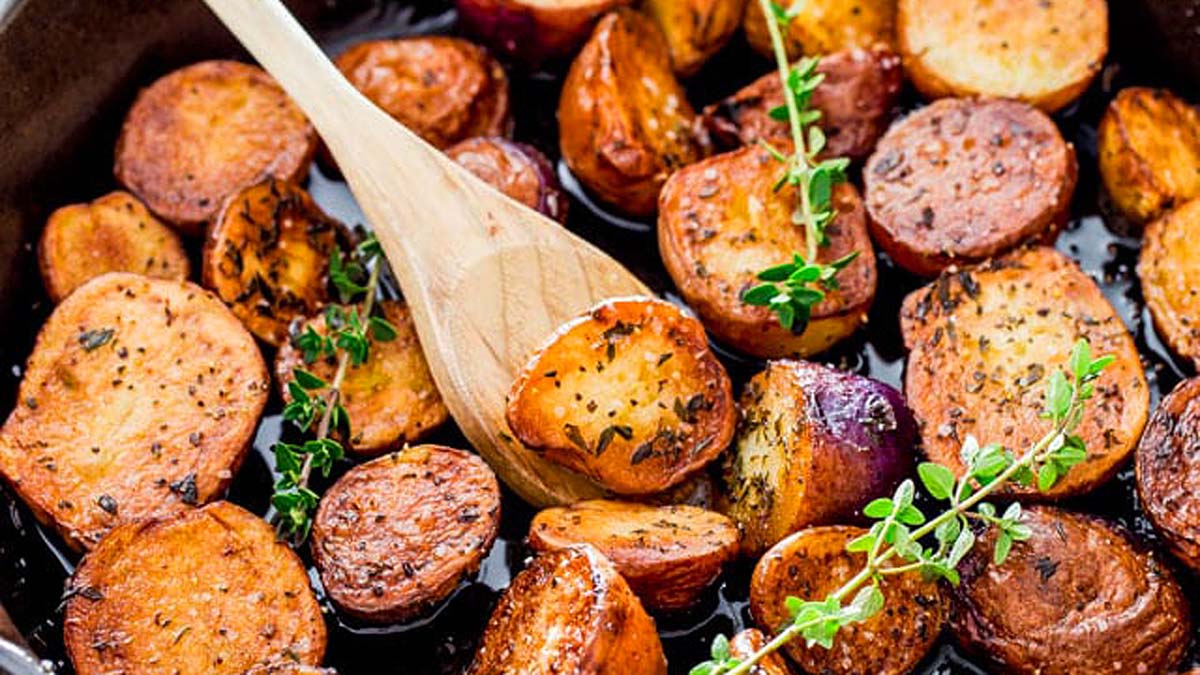 A skillet of roasted potatoes with a wooden spoon.