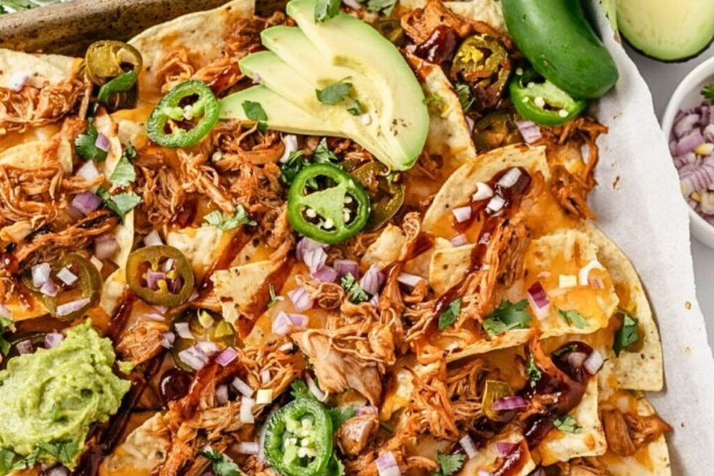A tray of nachos topped with peppers and bbq chicken.