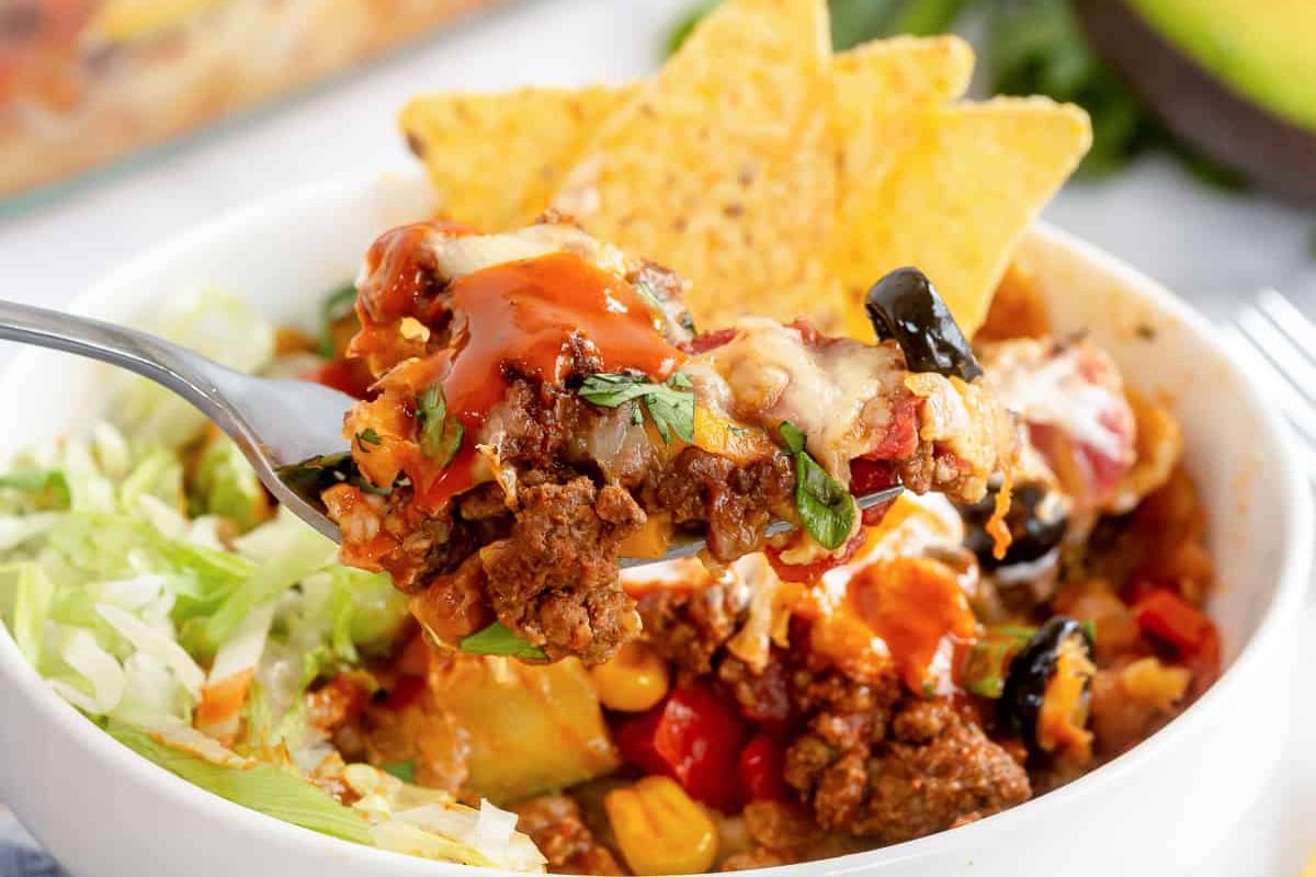 A casserole dish with taco casserole, topped with olives and green onions.